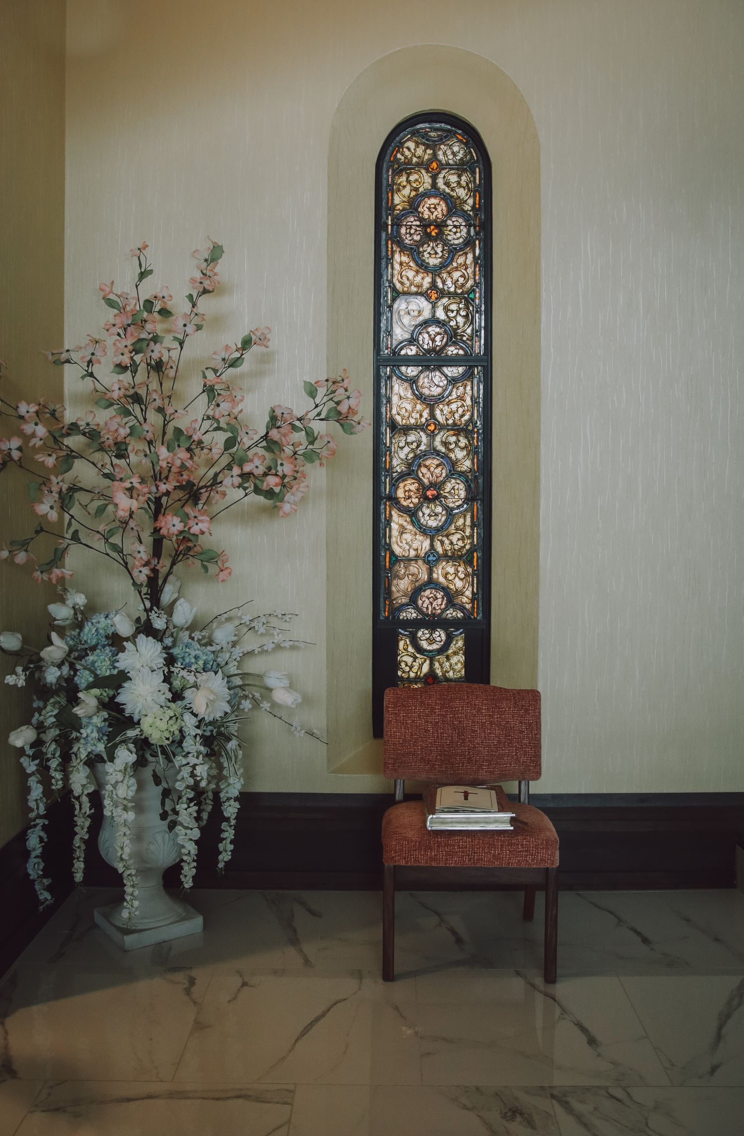 Decorative floral arrangement with pink and white blossoms sits beneath an ornate arched window with intricate metalwork.