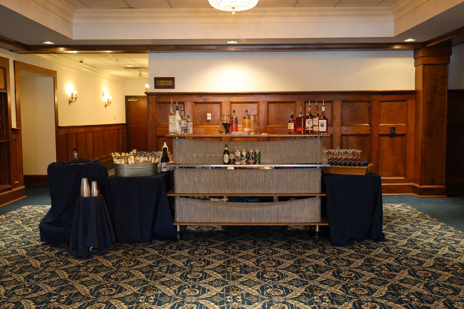 Elegant hotel banquet room with wood paneling, blue carpeting, and multiple serving stations along the walls.