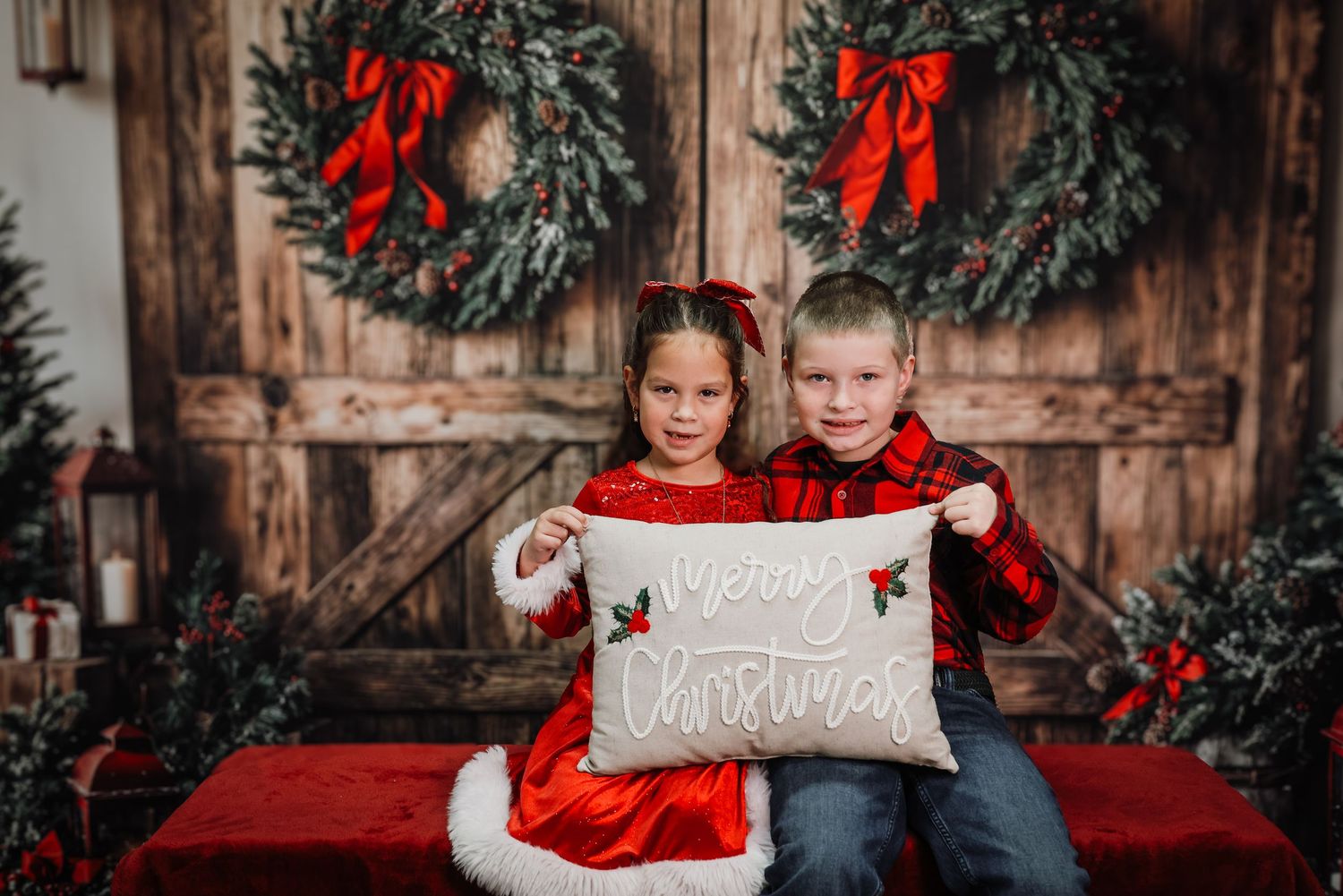 Christmas holiday photo session with evergreen wreaths, red bows, and rustic wooden backdrop decorations.