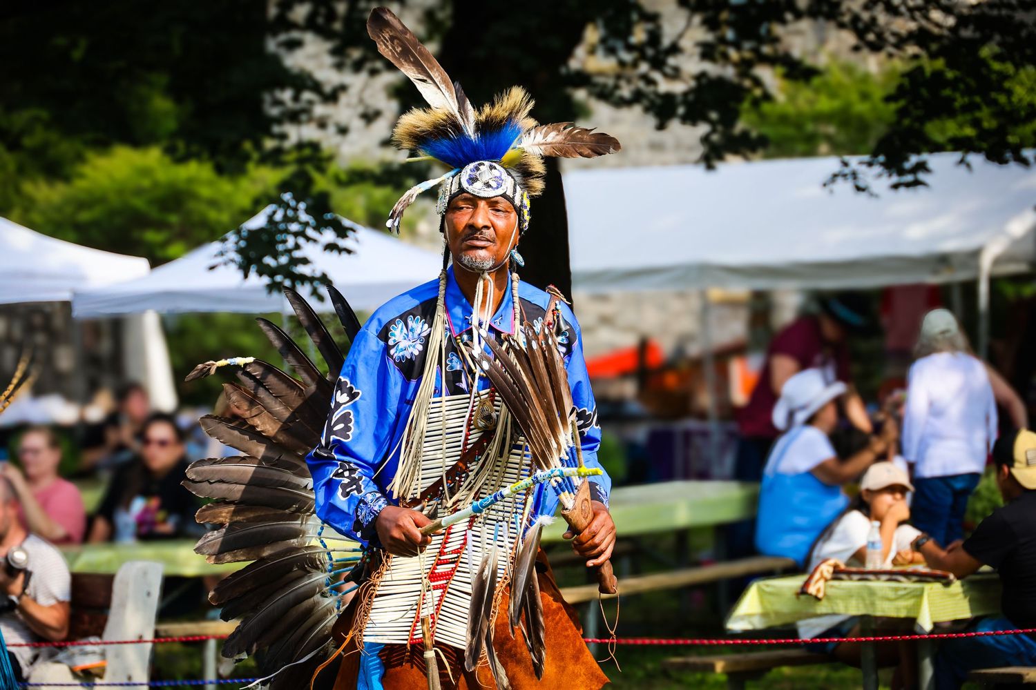 Traditional Native American dancer performs in vibrant blue regalia at outdoor cultural festival.