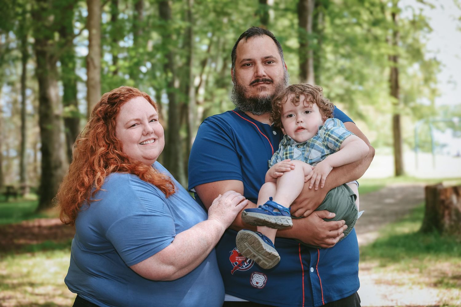 Three people in coordinating blue outfits pose together for a casual outdoor family portrait in a wooded setting.