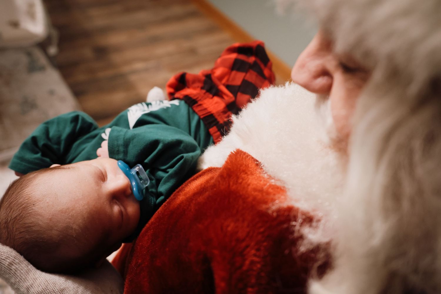 A newborn baby sleeps peacefully wrapped in a red and white blanket on a wooden surface.