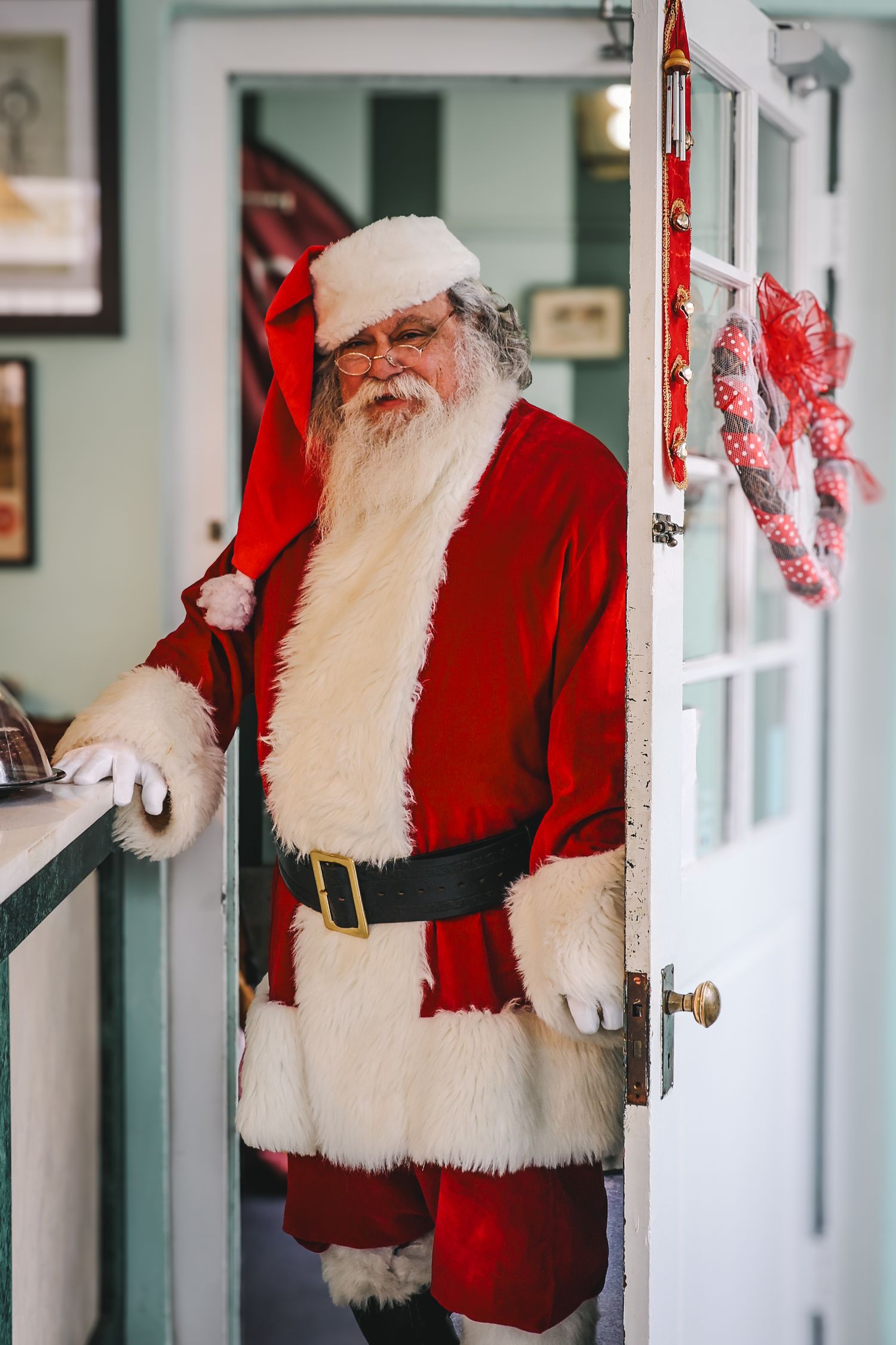 Multiple reflections of Santa Claus in white-framed mirrors showing traditional red suit and white beard.