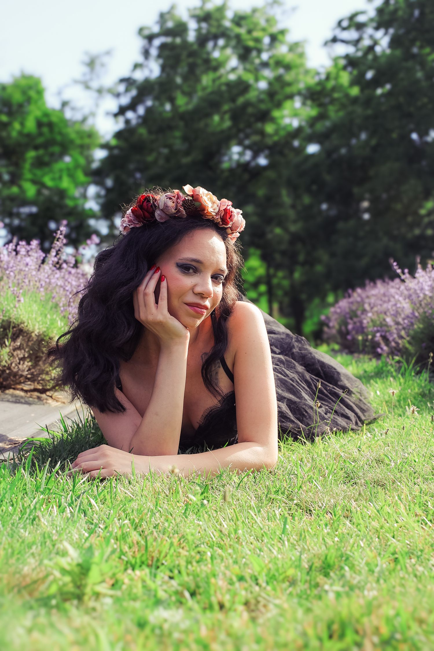 A person wearing a floral crown lies peacefully on green grass in a dreamy outdoor portrait setting.