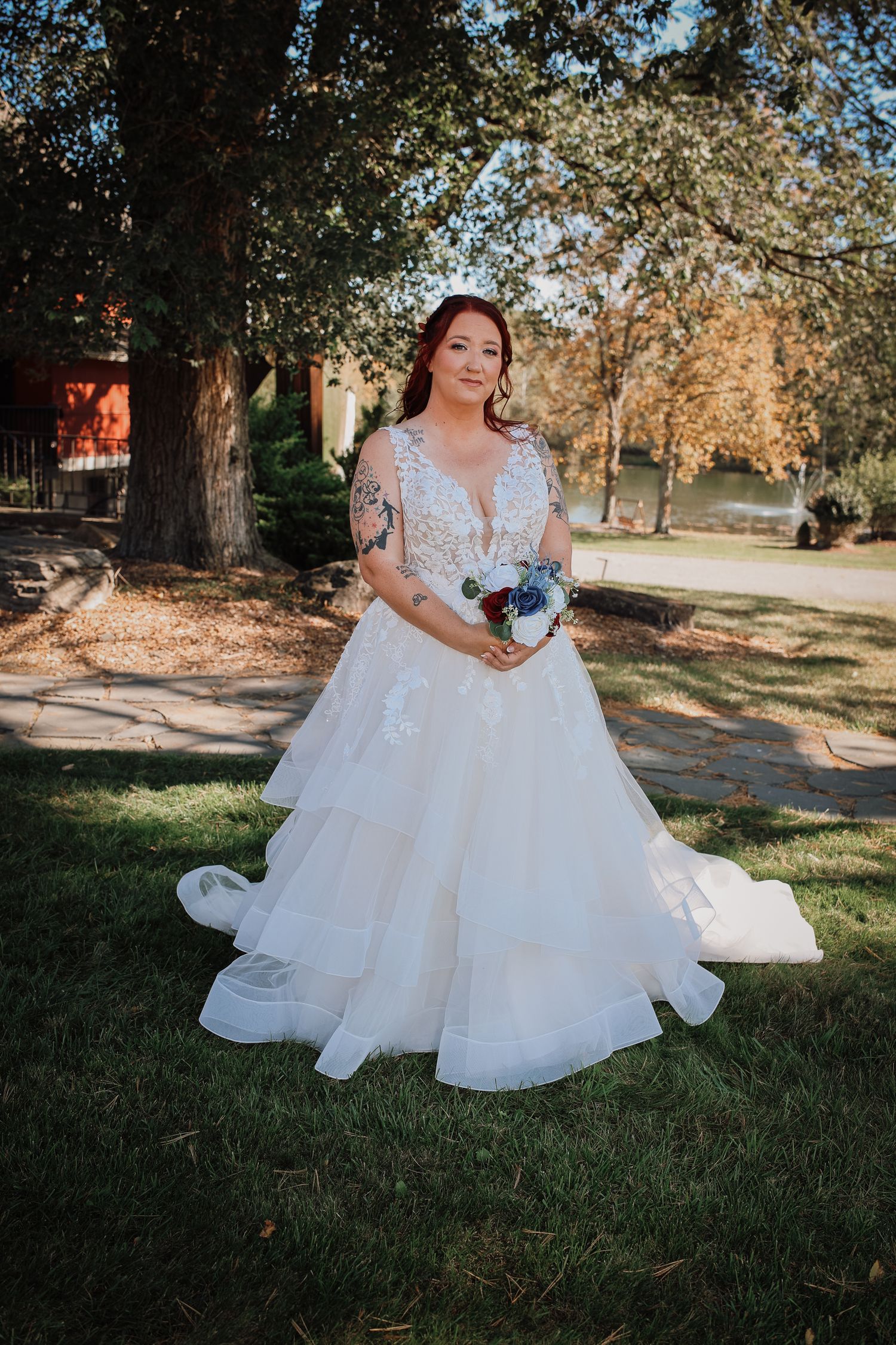 A person in a white lace wedding gown with flowing tulle skirt poses outdoors in an autumn garden setting.
