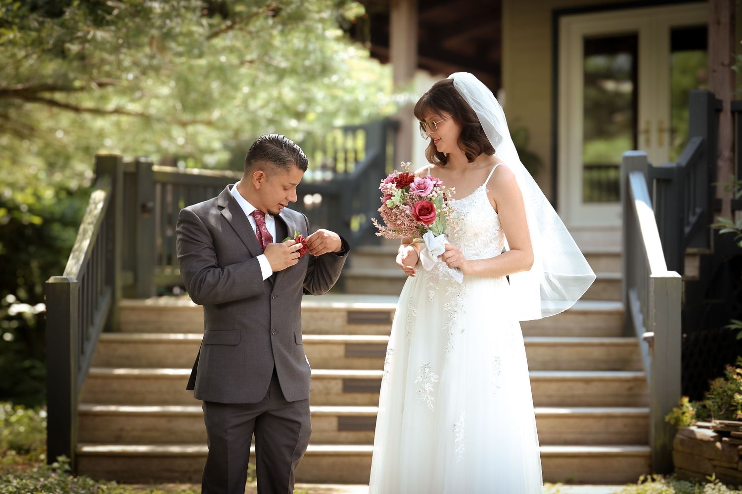 A bride in a white wedding dress and groom in a gray suit share a lighthearted moment on outdoor steps.