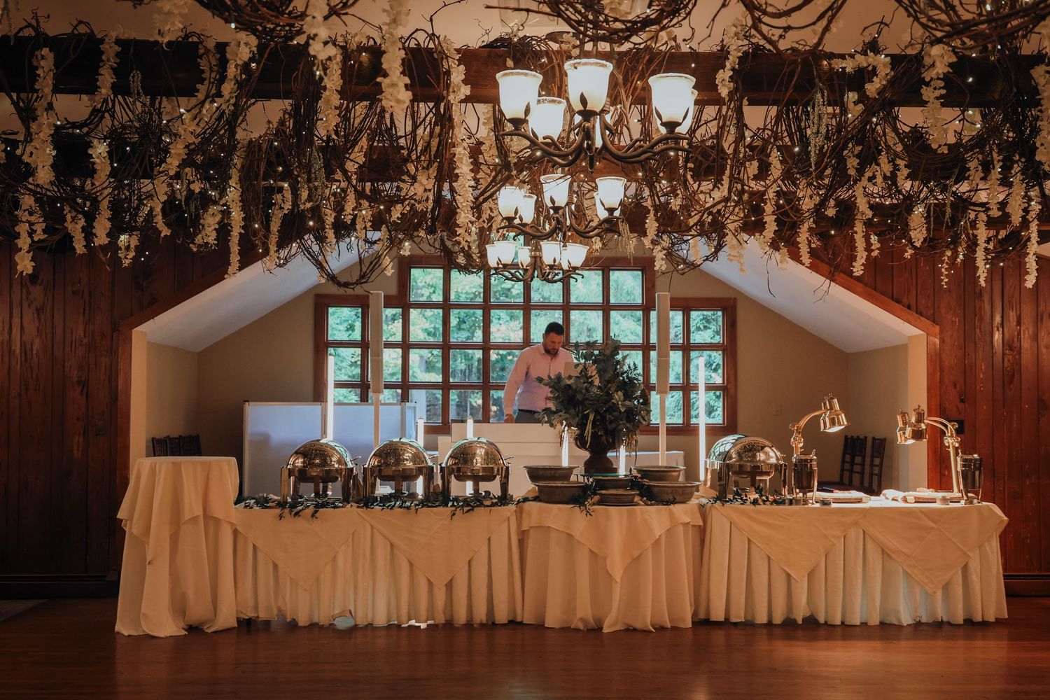 A rustic wedding reception venue with elegant chandeliers and white table settings in warm ambient lighting.
