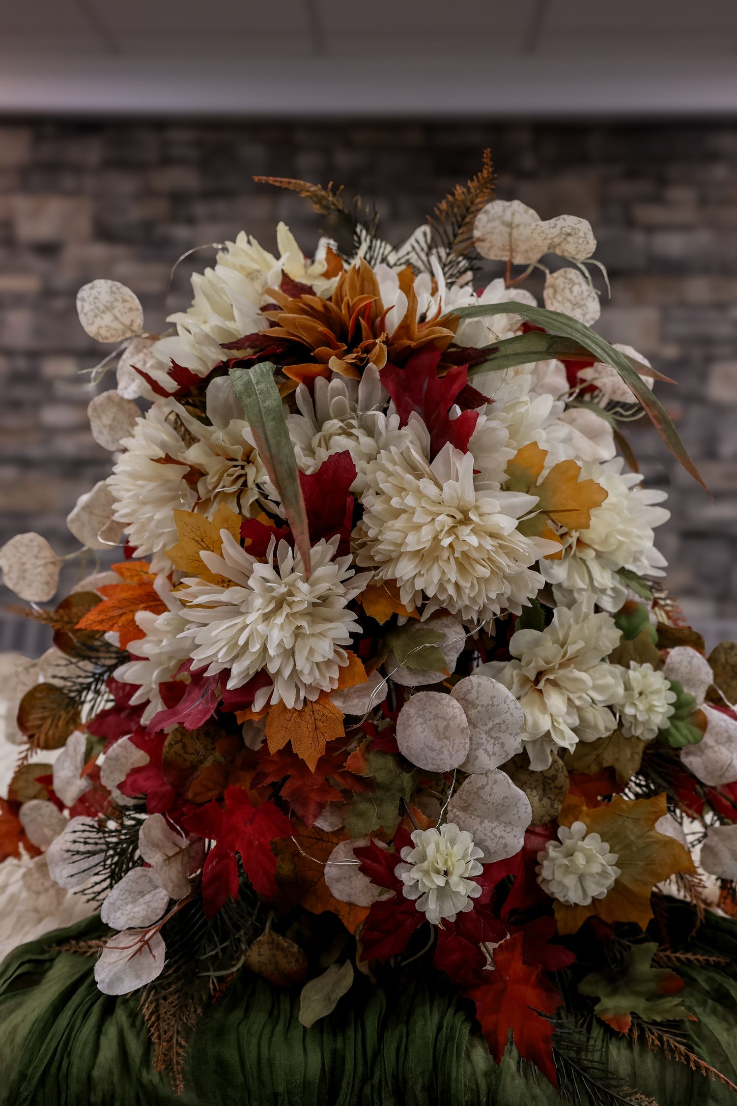 Close-up view of an autumn-themed floral arrangement with white chrysanthemums, burgundy flowers, and dried leaves.