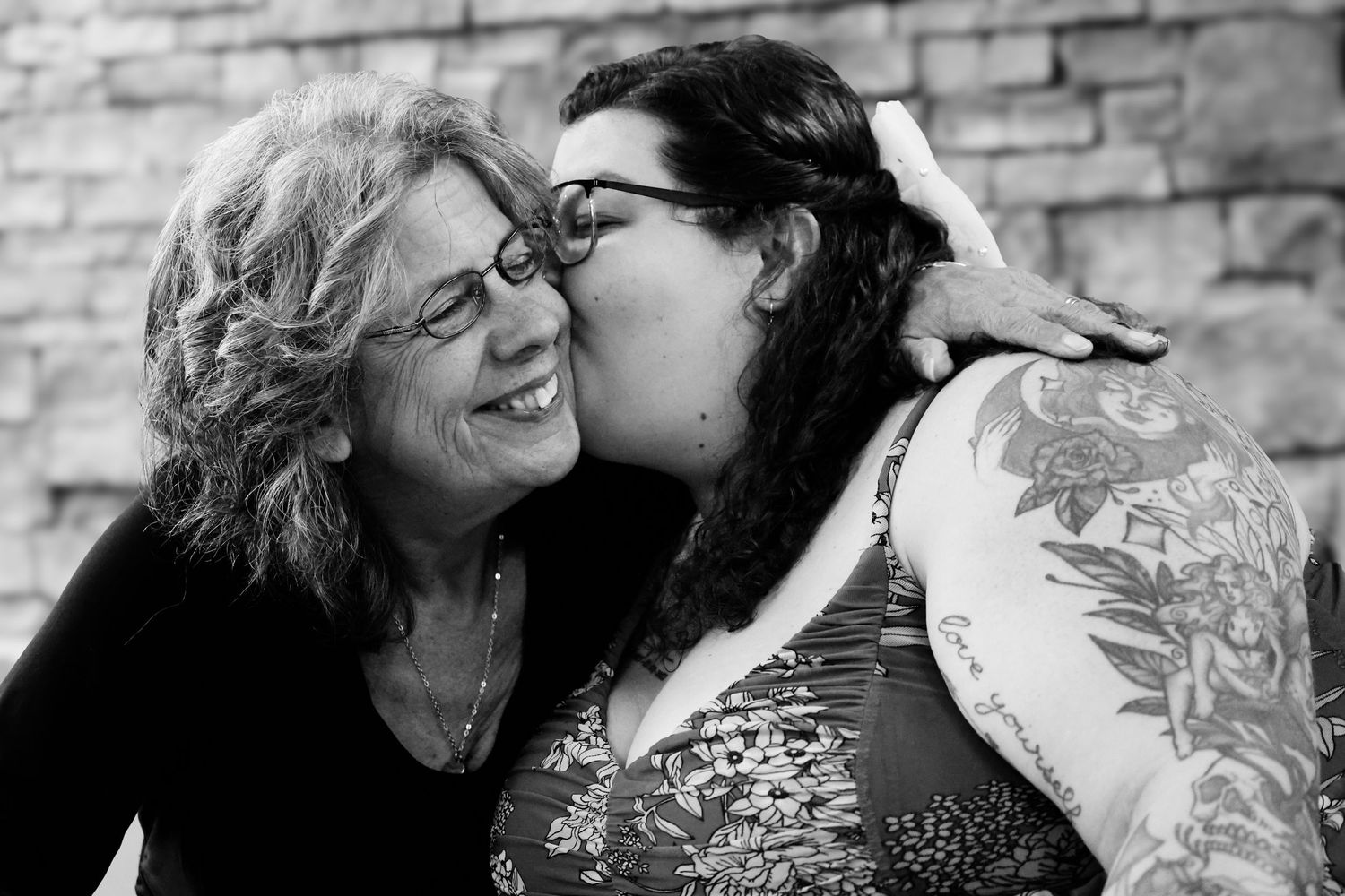 A tender moment between two people sharing laughter and affection against a brick wall background.