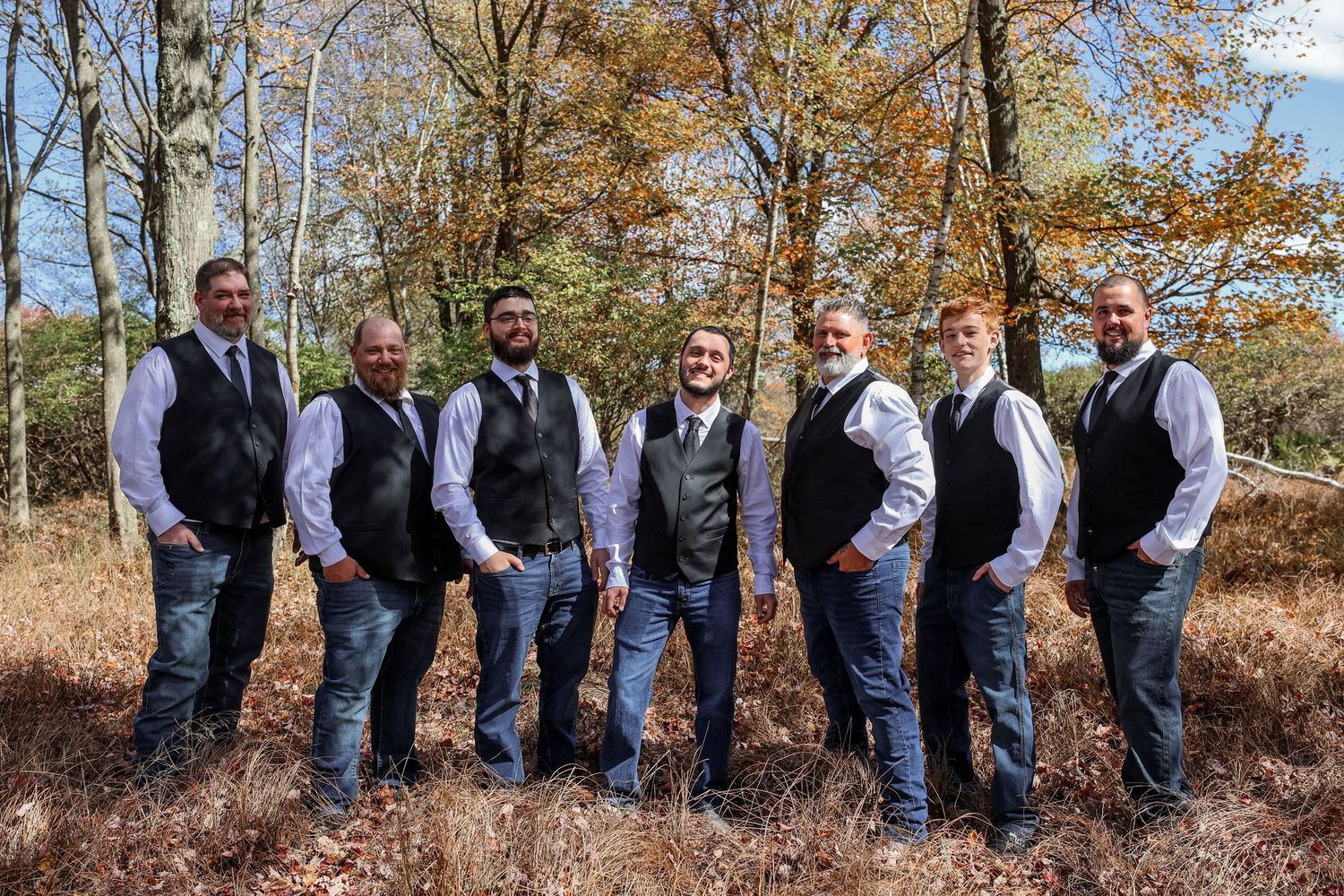 A row of groomsmen in gray vests and jeans pose for a creative photo sequence against autumn trees.
