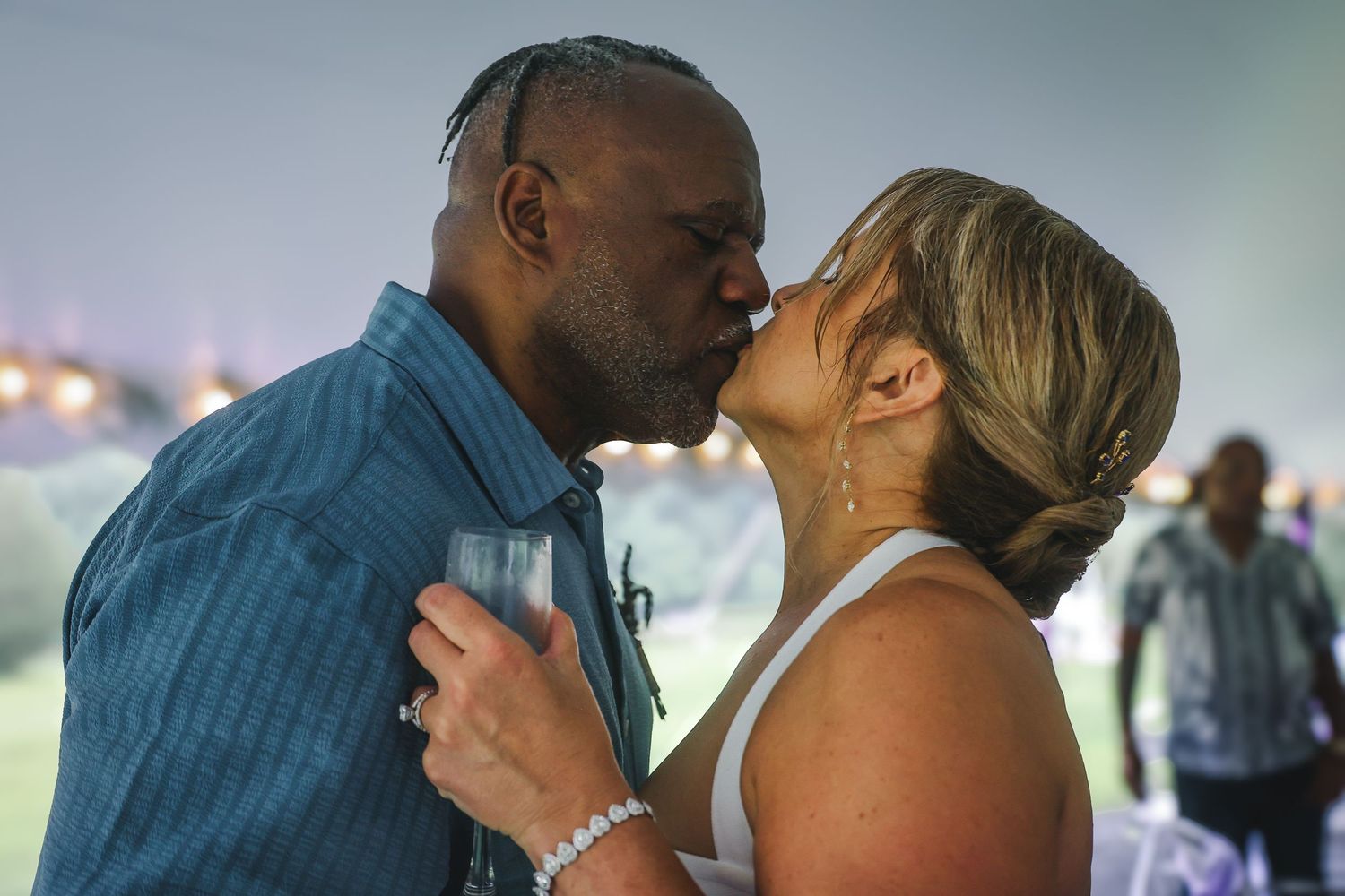 A couple shares a romantic dance moment at an evening celebration with soft lighting in the background.