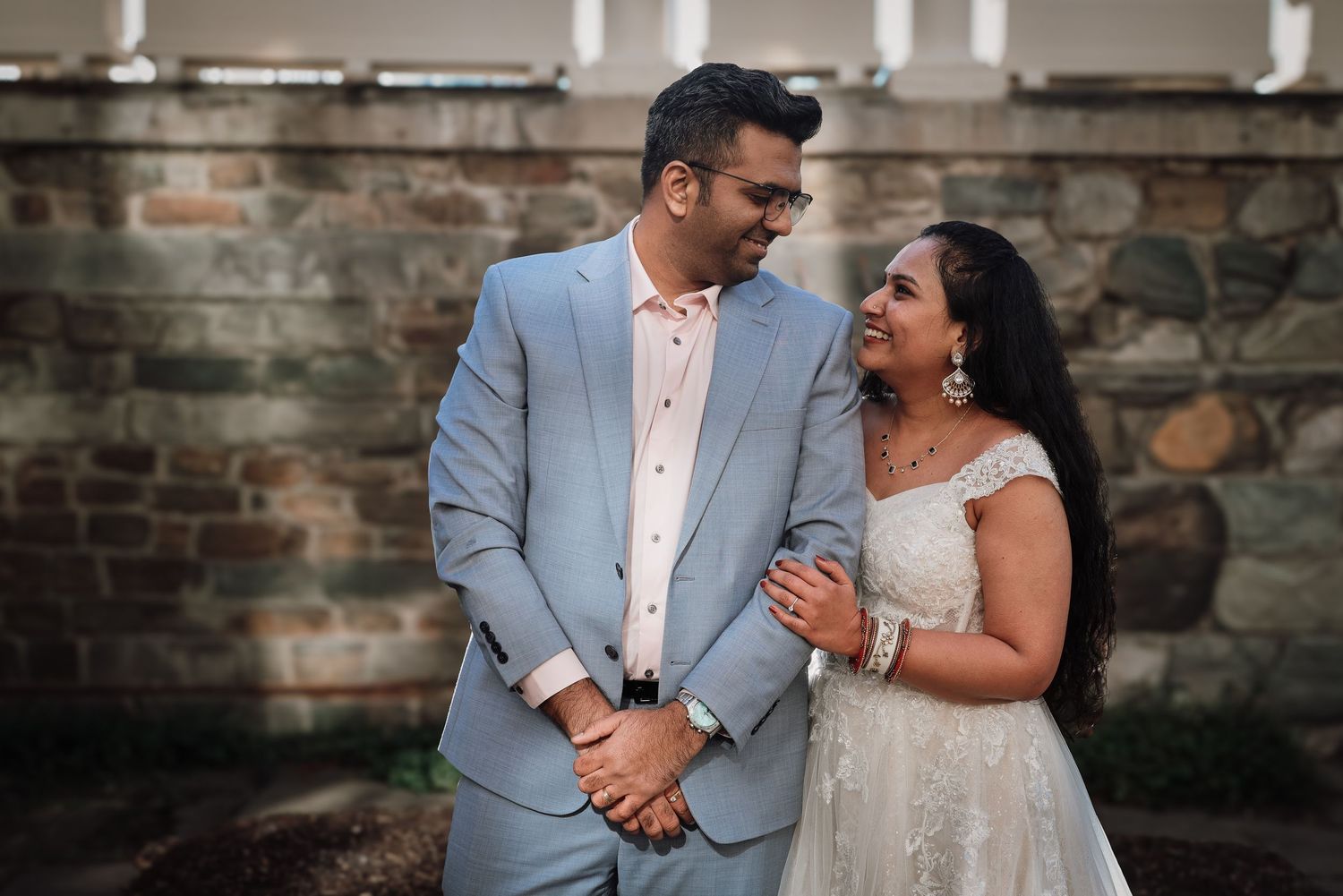 A couple shares intimate moments against a rustic brick wall backdrop during their wedding photoshoot.