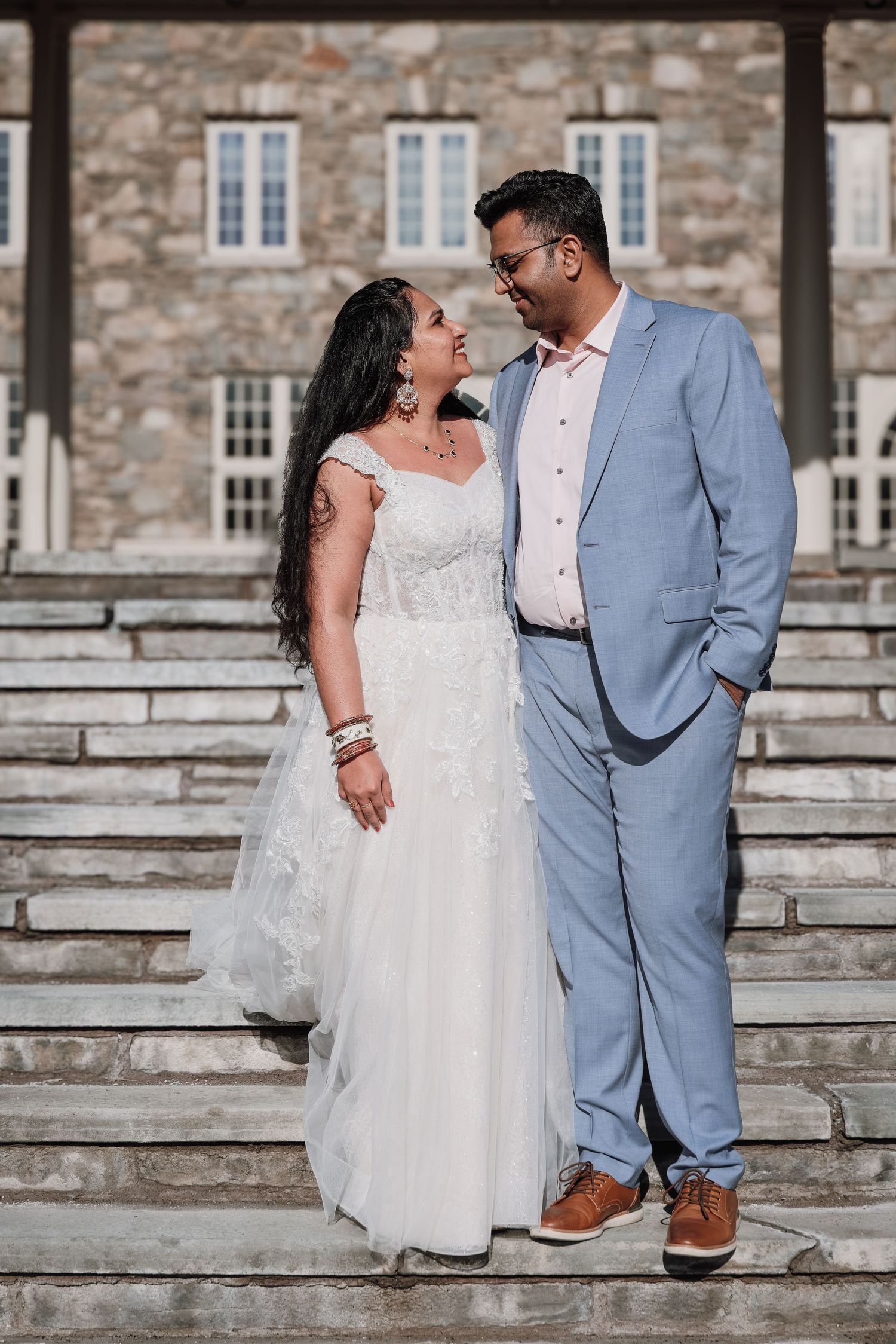 A couple in wedding attire shares intimate moments on stone steps outside a historic building.