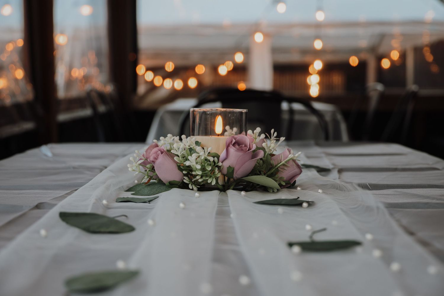 Elegant wedding reception table settings with string lights overhead and soft pink floral centerpieces.