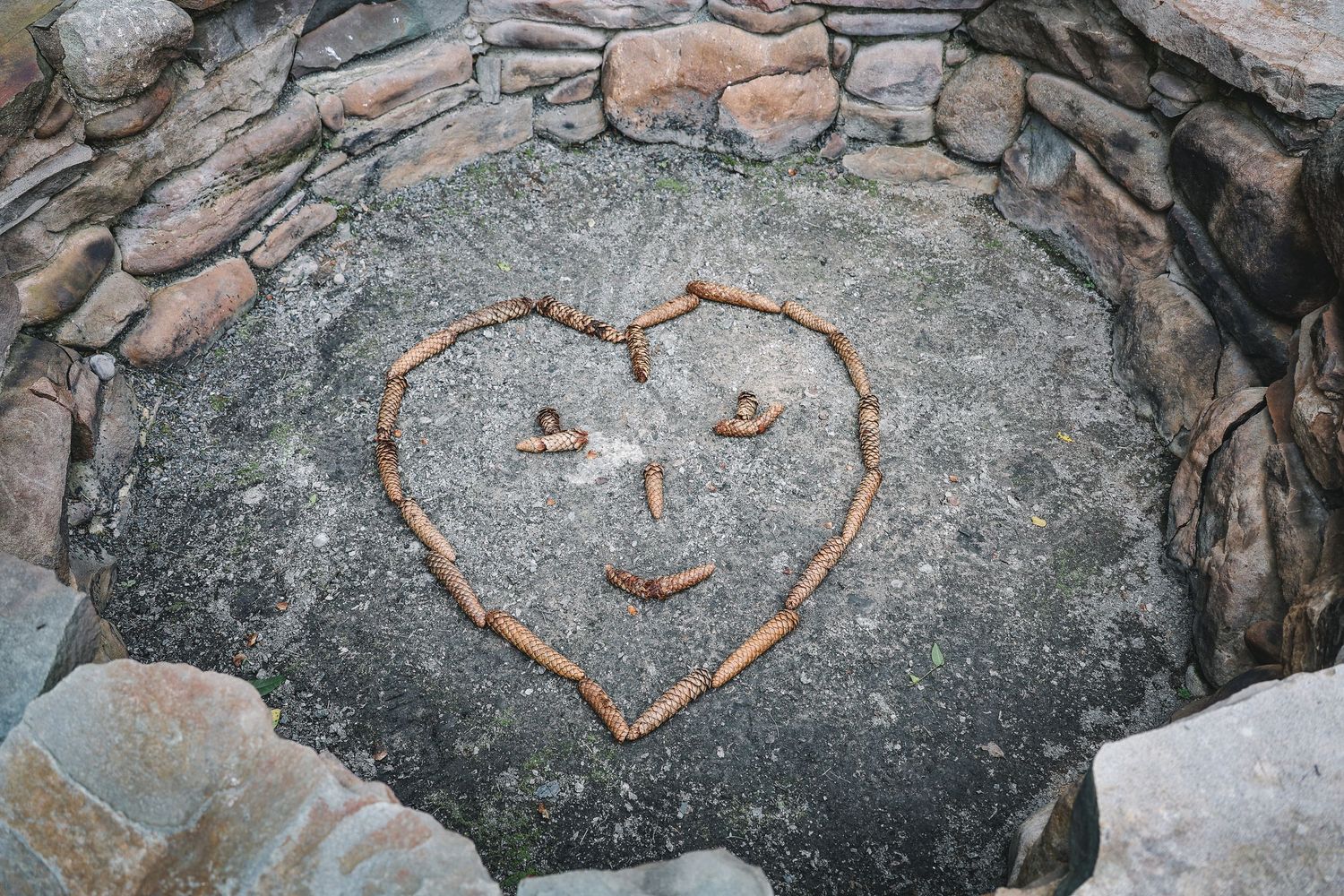 A heart-shaped smiley face made from twigs on a large stone surrounded by a rock border.