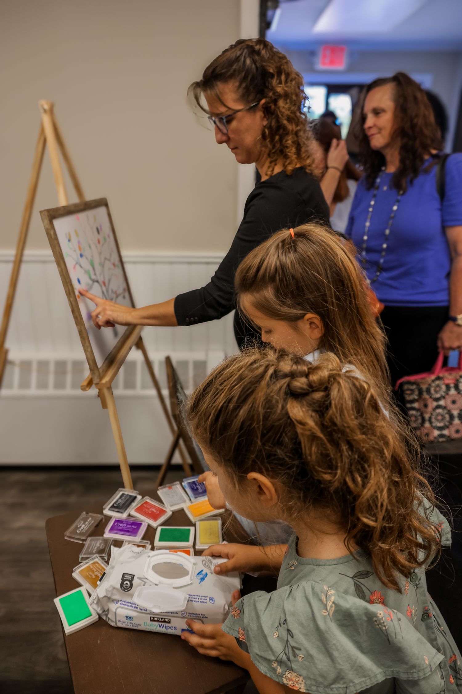 Art students gather around supplies and an easel during a creative workshop with colorful ink pads and art materials.
