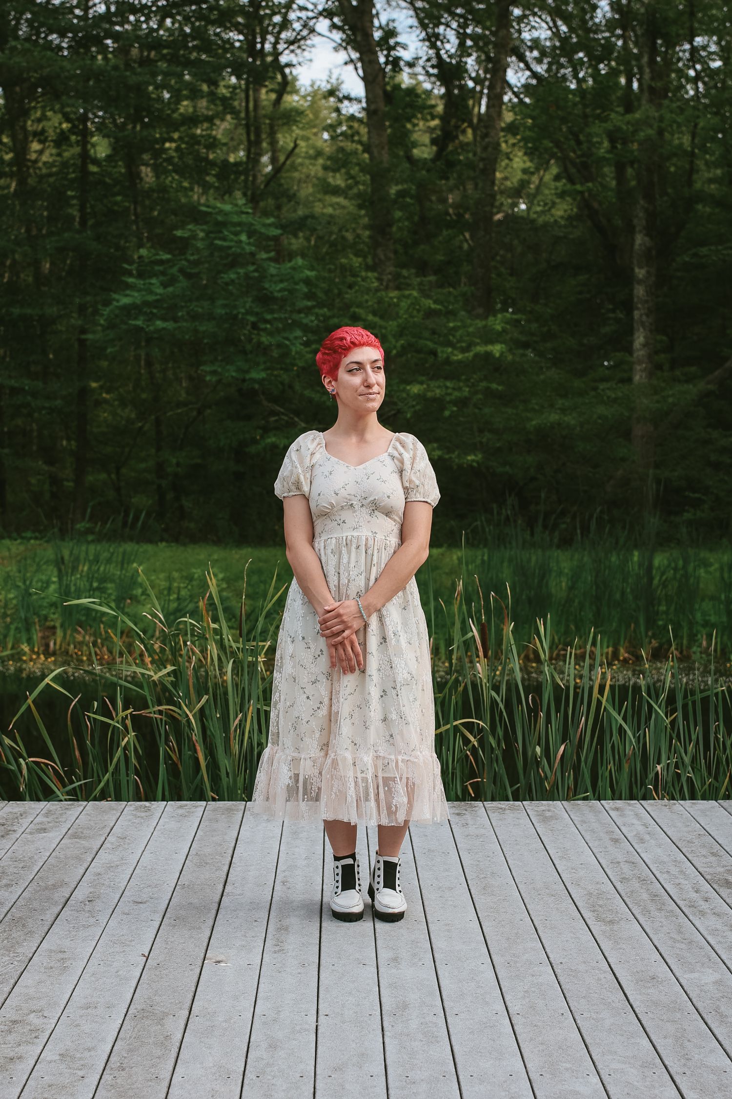 A wooden boardwalk extends through lush green forest scenery with someone in a vintage-style white dress.