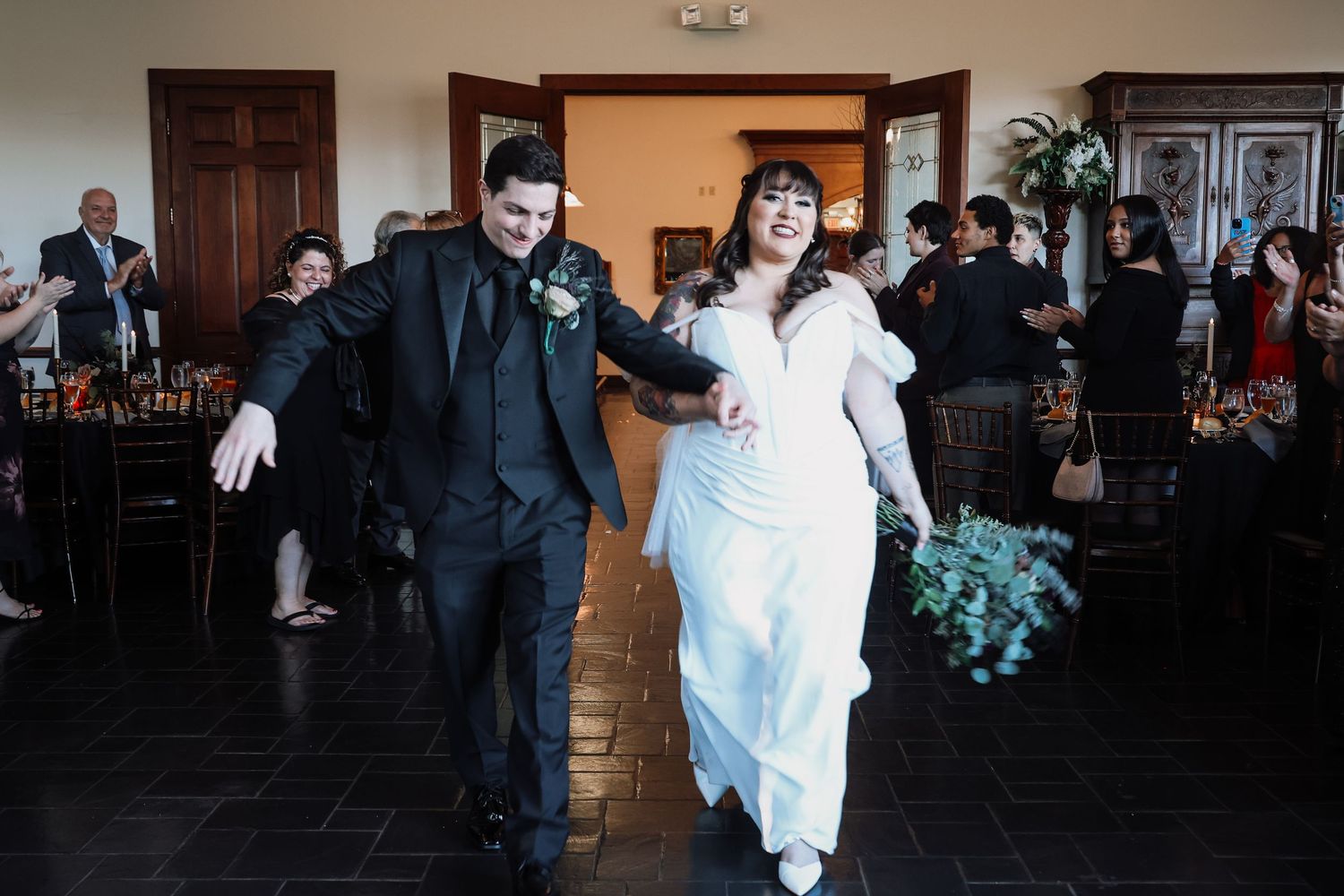 A joyful couple enters their wedding reception venue with excited expressions and celebratory gestures.