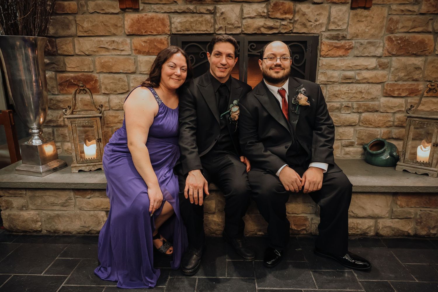 Wedding party members pose together against a rustic stone wall backdrop during an outdoor celebration.