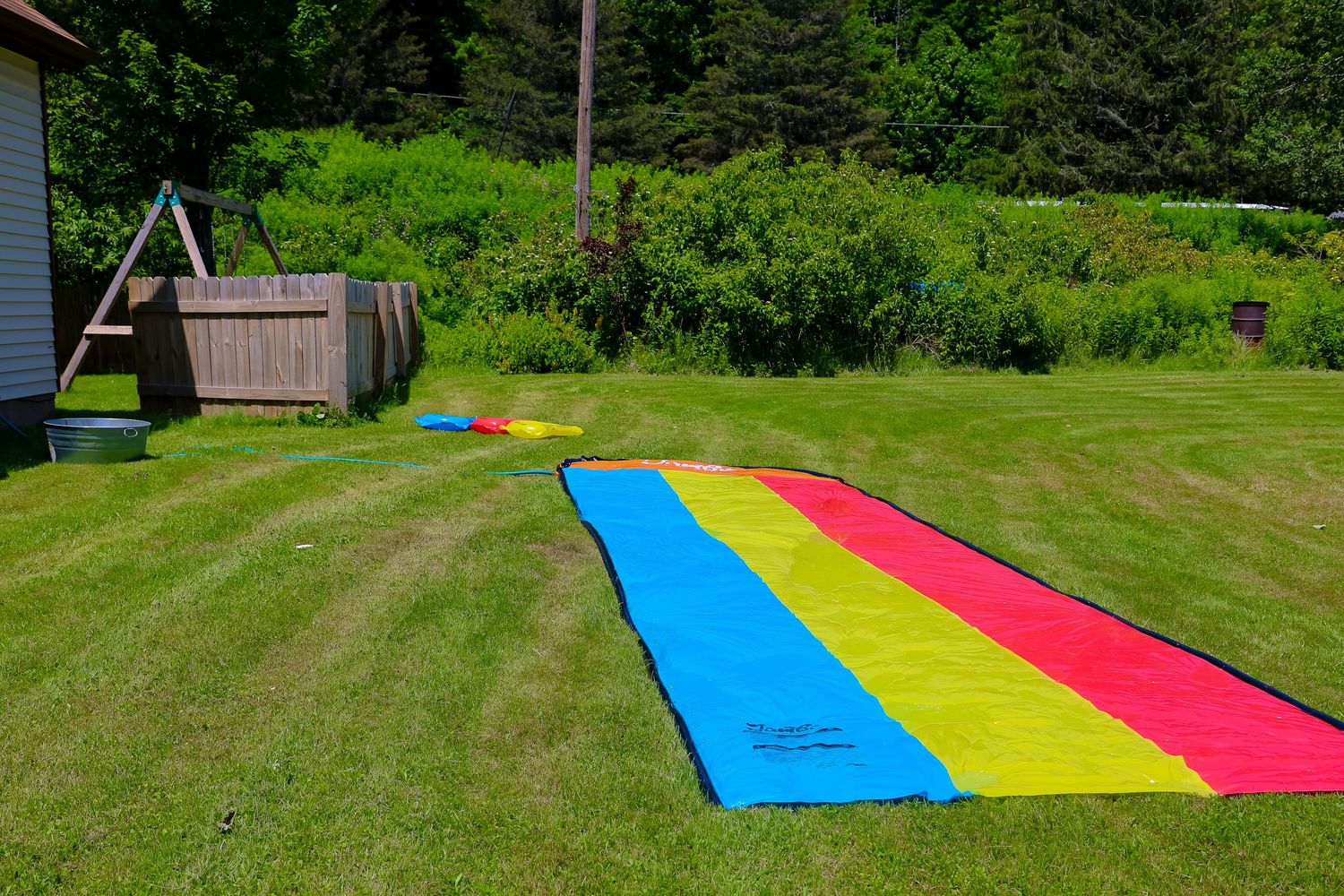 Colorful slip and slide set up on a grassy backyard hill with evergreen trees in the background.
