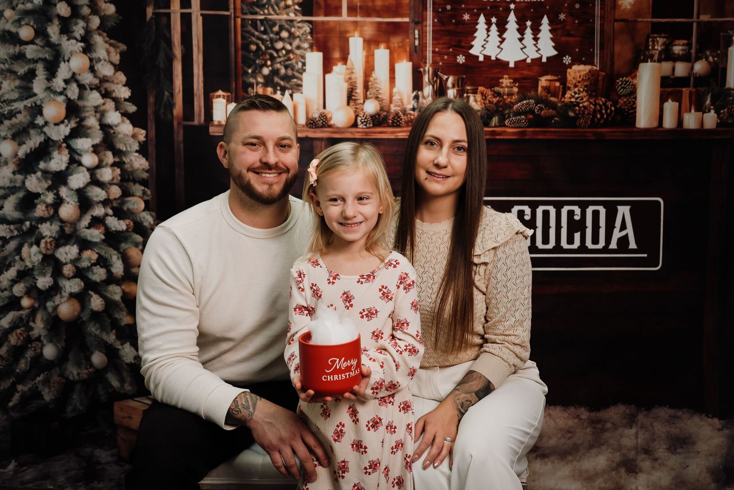 A family wearing coordinated white and red outfits poses together for holiday photos in front of a rustic backdrop.