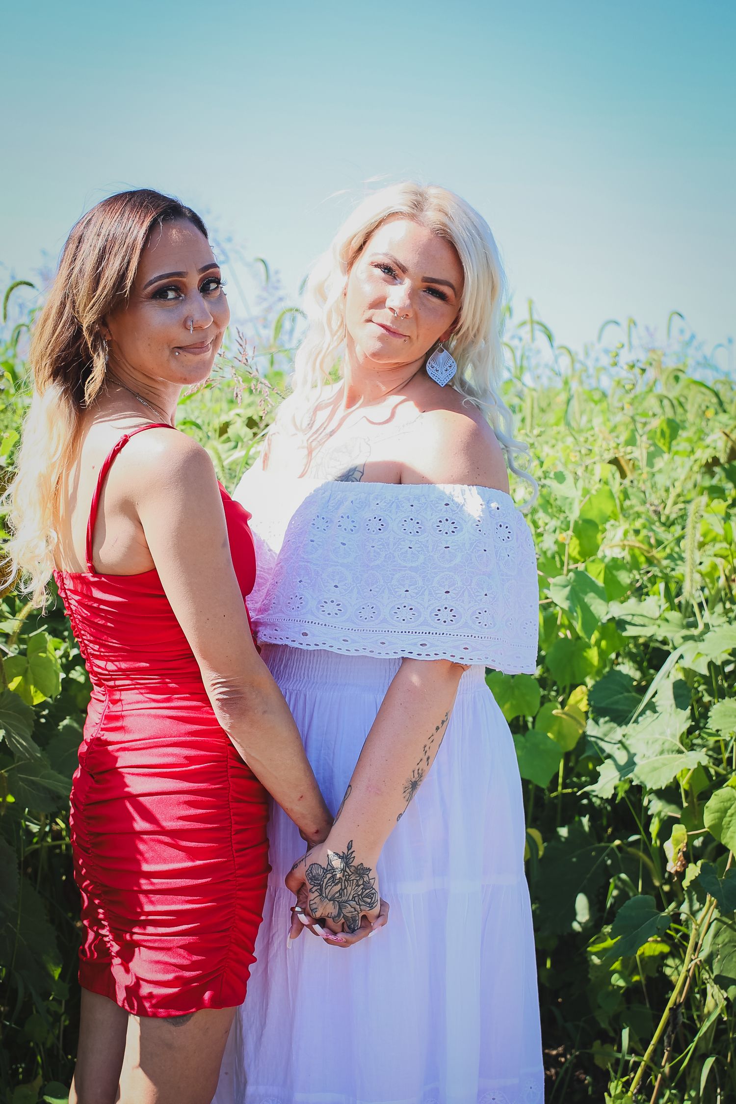 Two friends pose together in vineyard wearing contrasting red and white summer dresses.