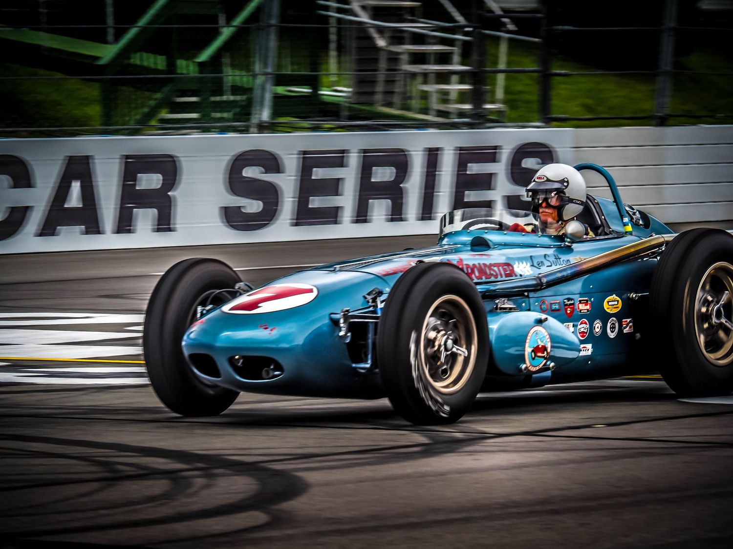 A vintage blue Formula 1 race car speeds around a track during a classic car competition event.