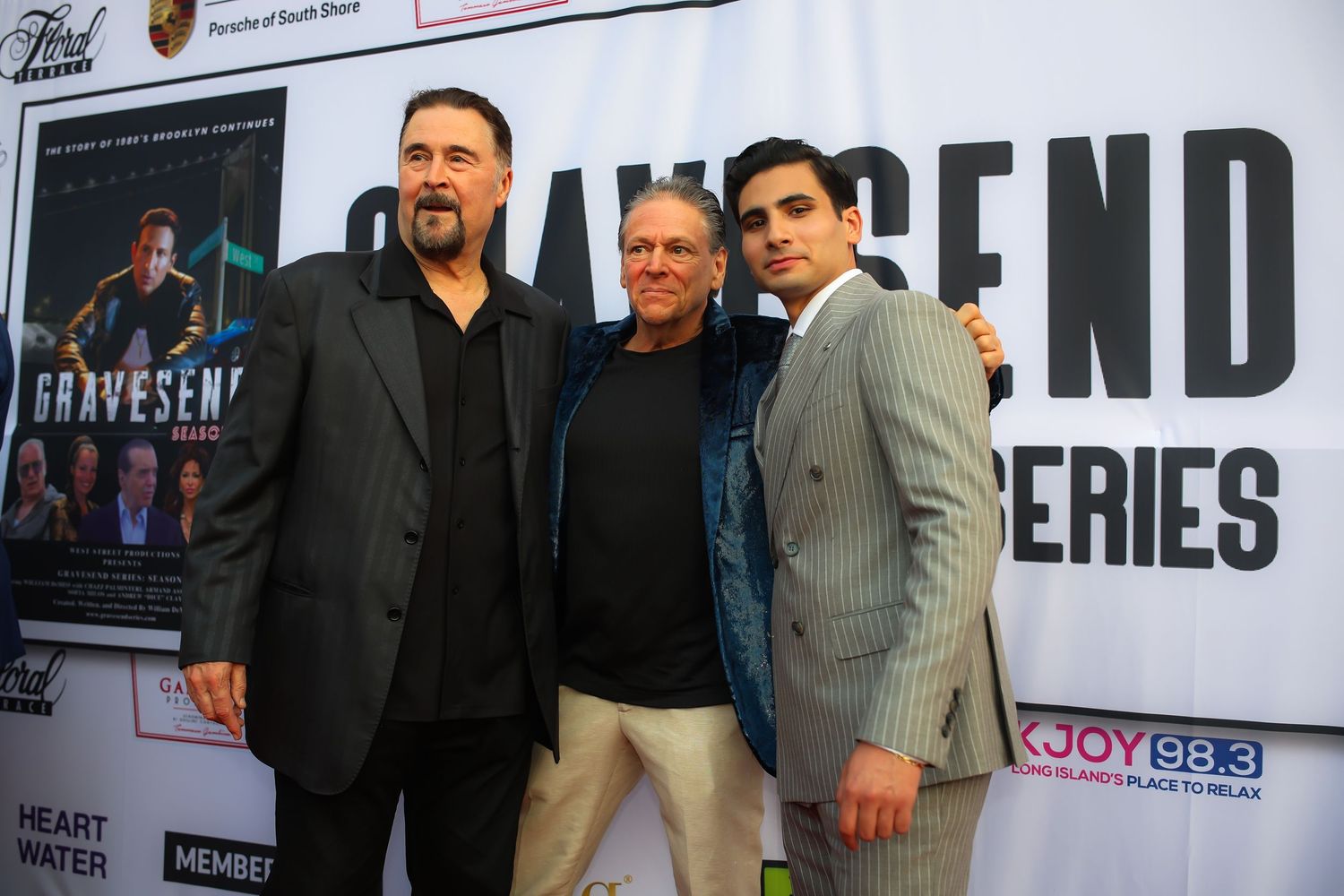 People posing together at a red carpet event wearing suits and formal attire.
