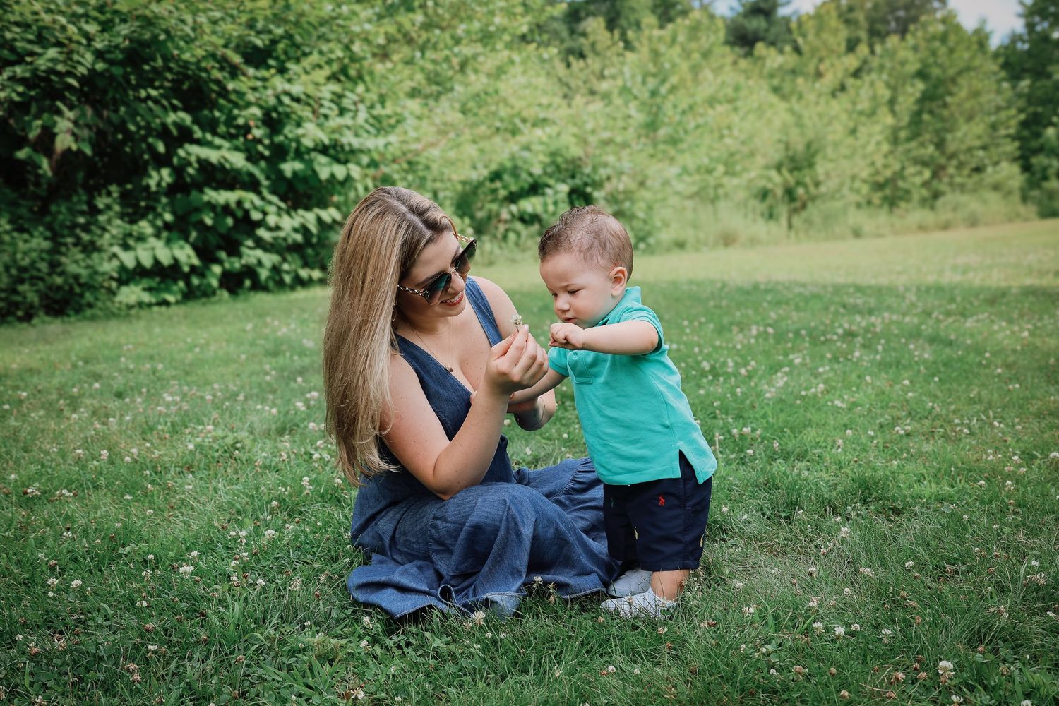 Parent and child sit together in a lush green field on a sunny summer day.