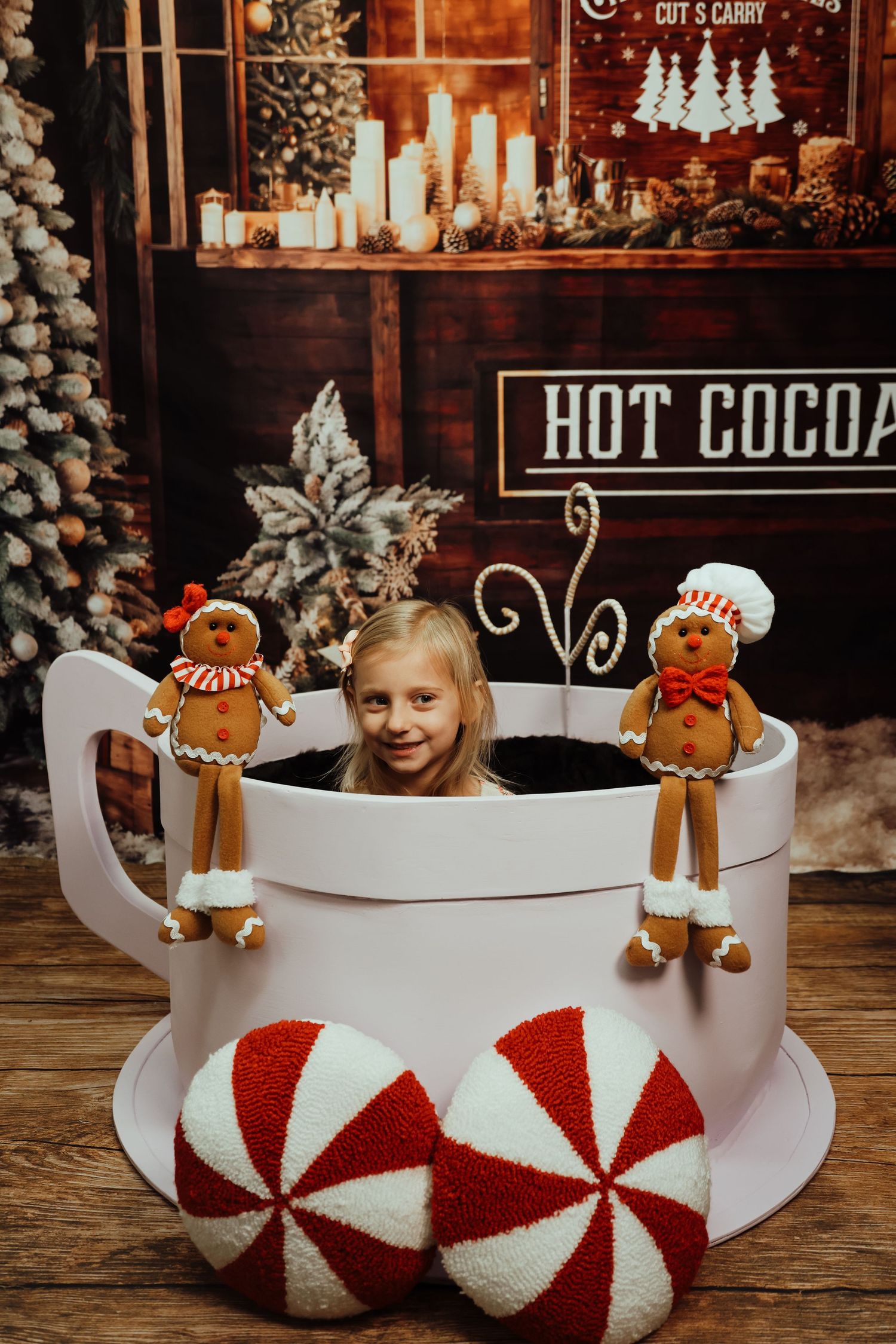 Children peek over edge of large white sleigh prop with red peppermint candy design and gingerbread decorations.
