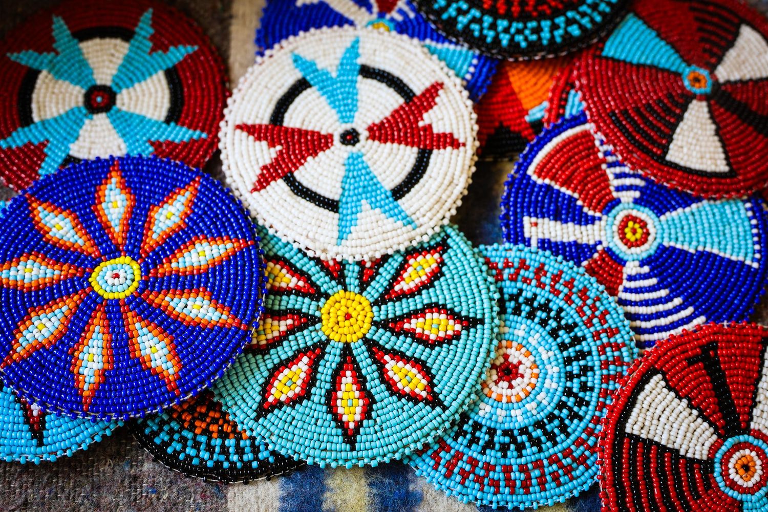 Colorful Native American beaded medallions and rosettes featuring geometric patterns in red, white, and turquoise blue.