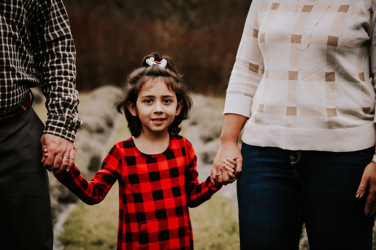 A family wearing plaid and casual clothing holds hands while walking together outdoors.