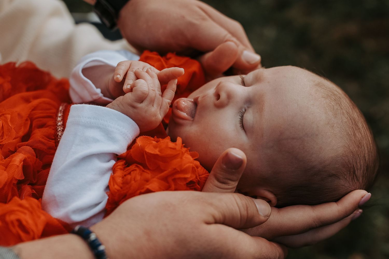 A sleeping baby wearing orange and white clothing lies on a dark background.