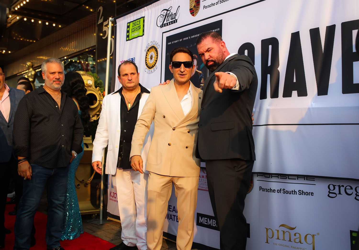 People in formal attire pose together on a red carpet at an entertainment industry event with signage in the background.