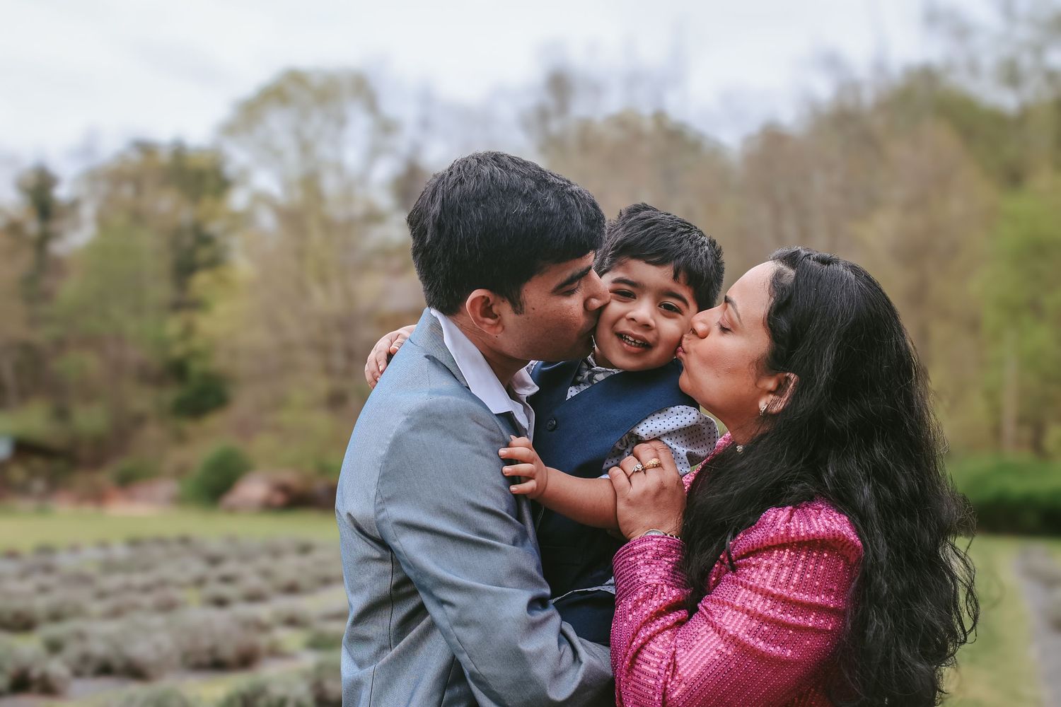 A family shares a joyful moment together outdoors in front of trees and shrubs on a spring day.