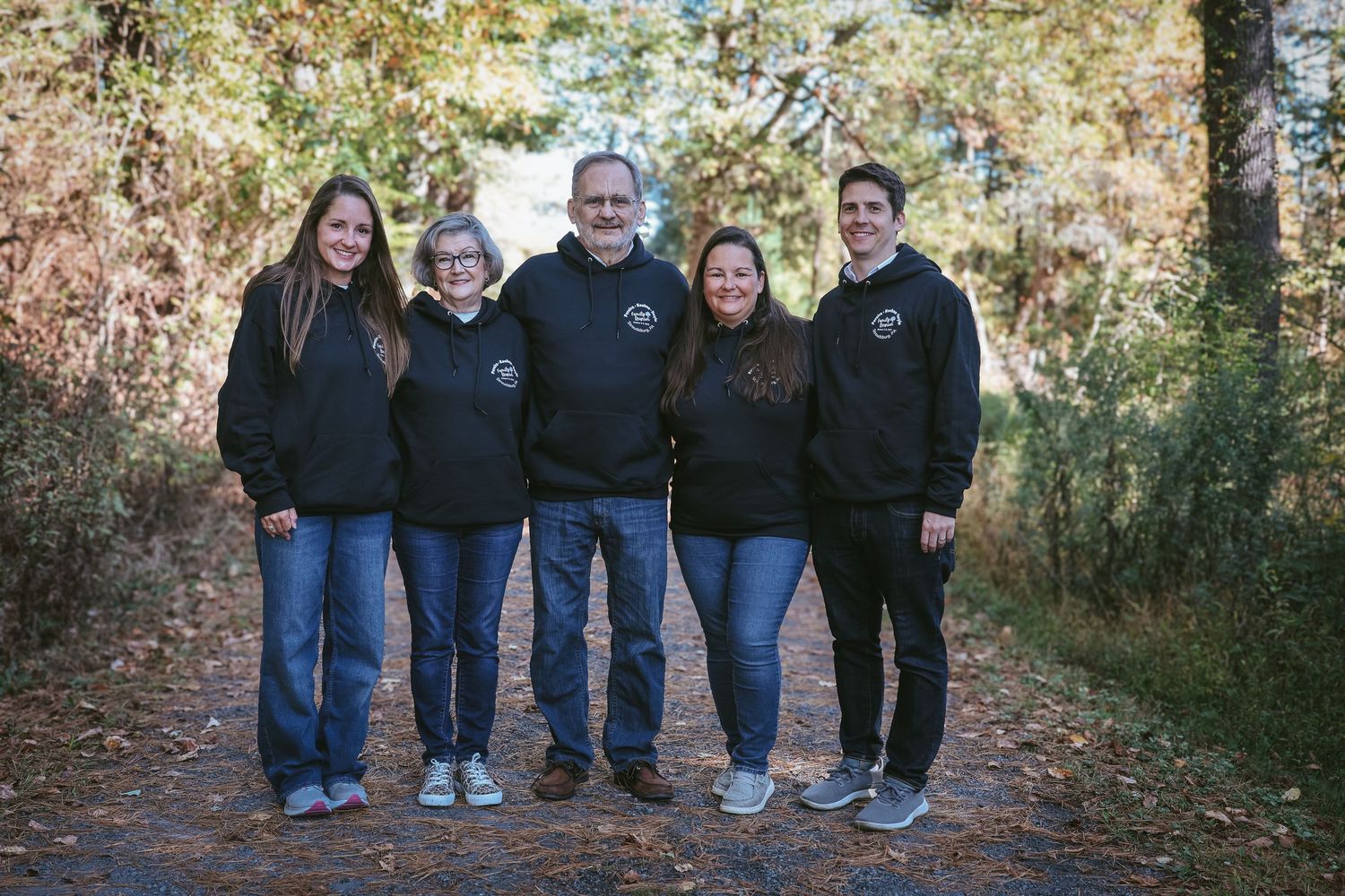 A group wearing matching navy jackets and jeans poses together on a leaf-covered path during autumn.