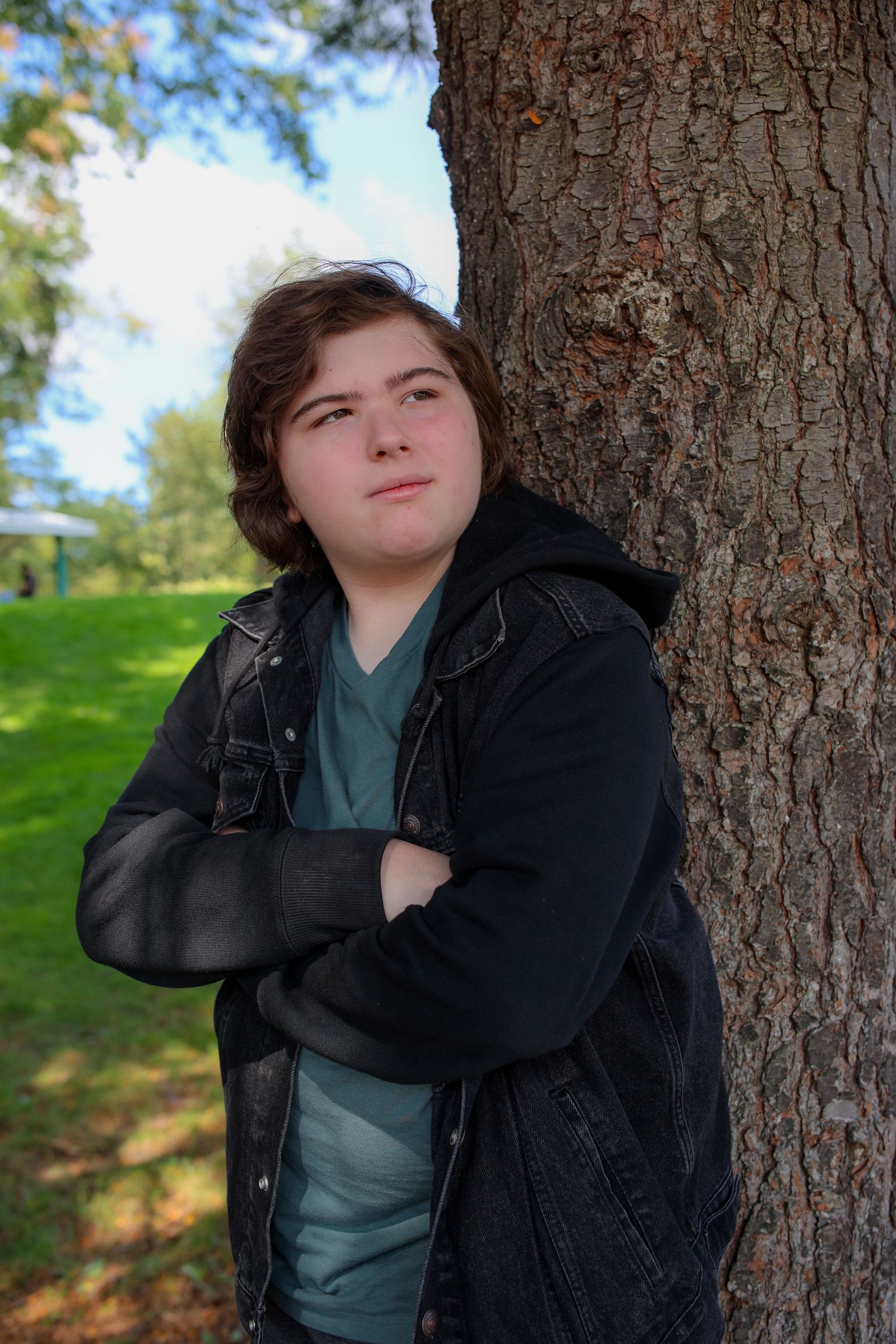 Person in black jacket poses against a tree trunk in a park setting across multiple similar shots.
