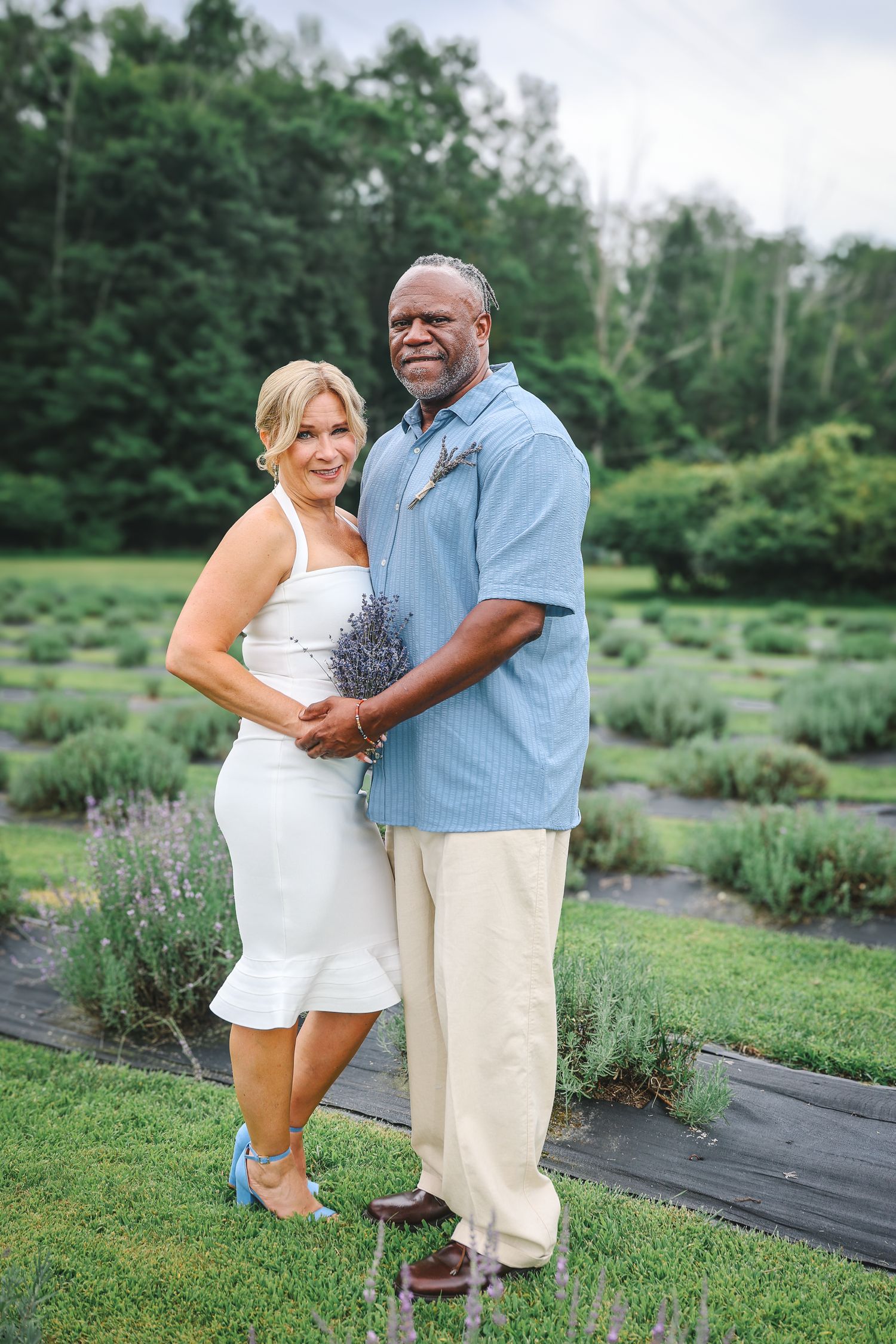 Couple posing together in a garden with blooming lavender plants and greenery.