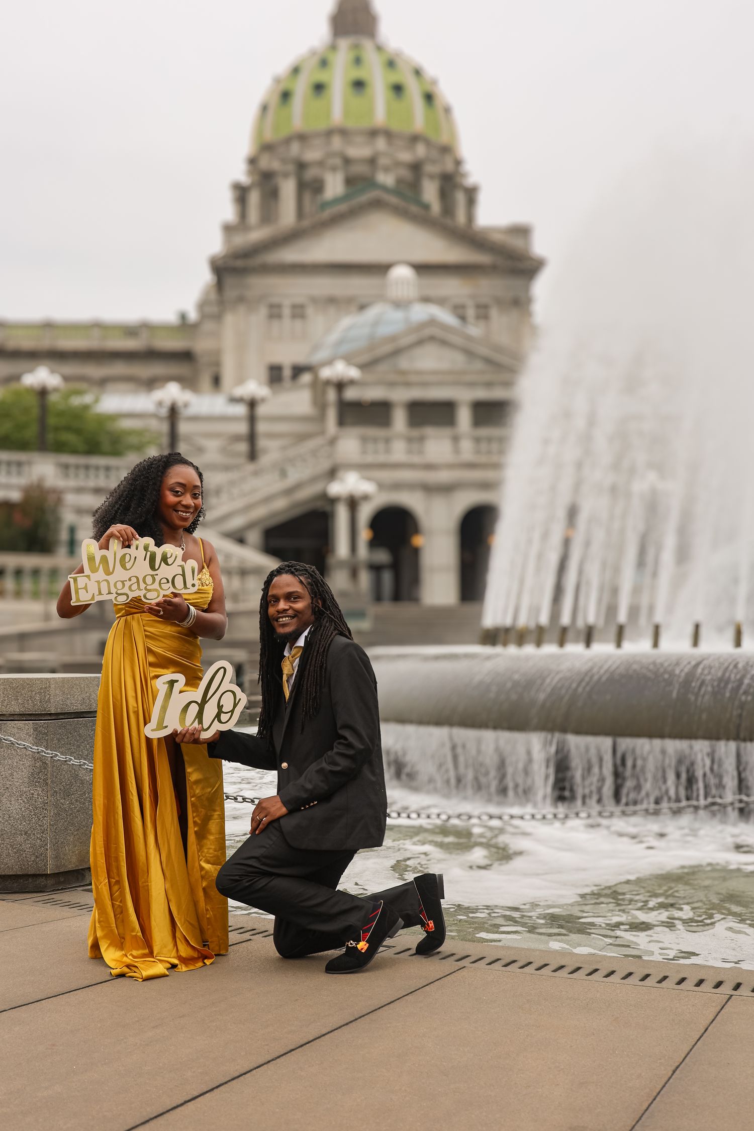 A couple poses together in front of the Pennsylvania State Capitol building and fountain in Harrisburg.