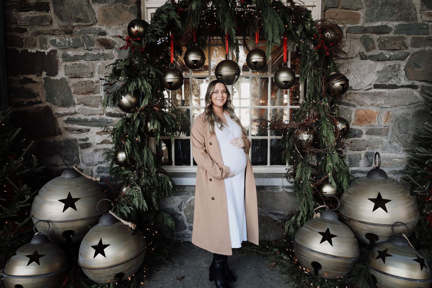 A festive holiday scene with stone walls, large silver bells, greenery and black star decorations creating a rustic Christmas display.