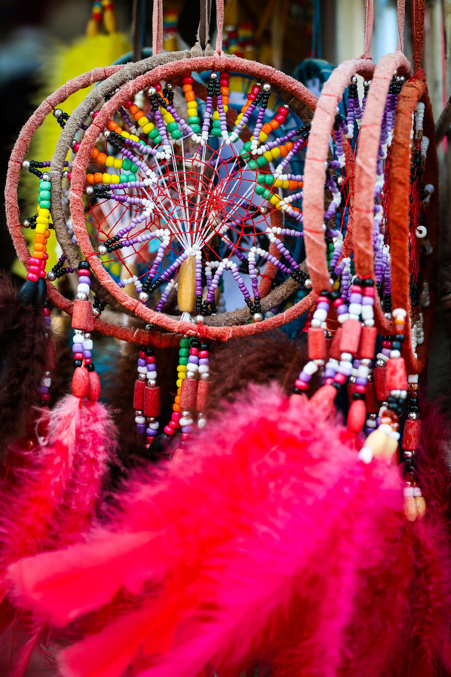 Colorful Native American dreamcatchers with bright red feathers and beaded decorations hanging at a market display.