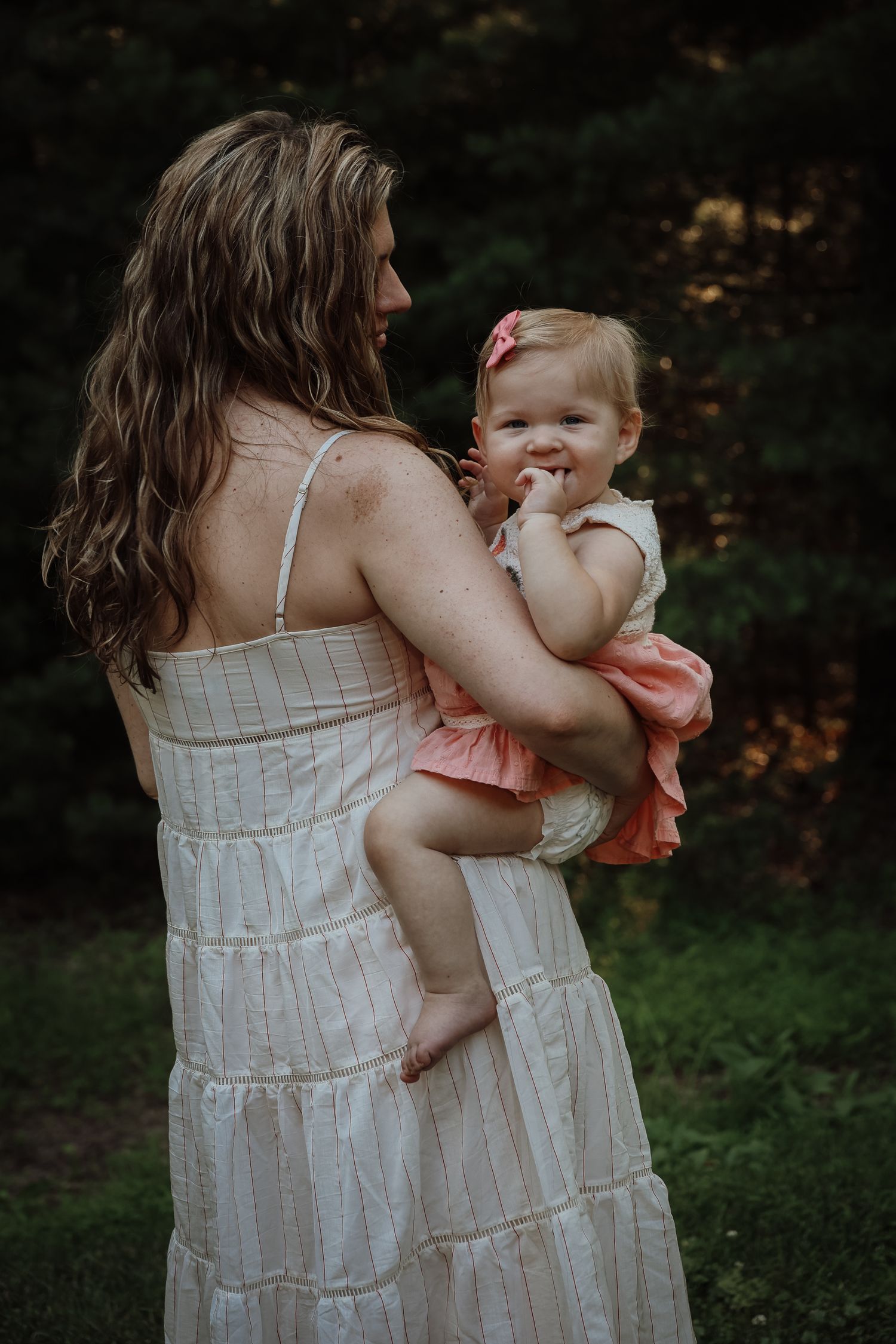 A tender embrace between parent and child wearing white dresses in a garden setting at dusk.