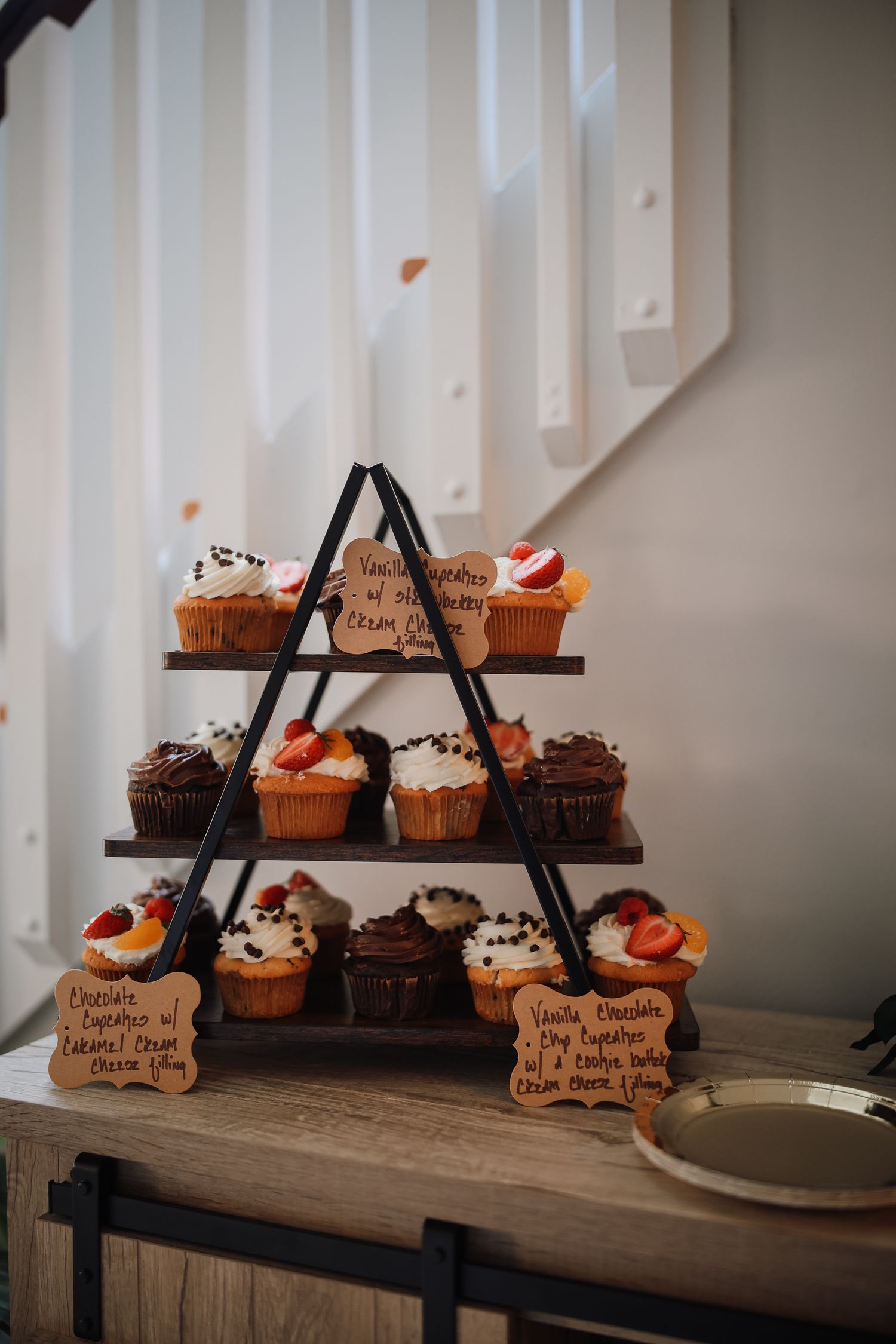 Artisanal cupcakes displayed on a rustic wooden tiered stand with handwritten labels and decorative details.