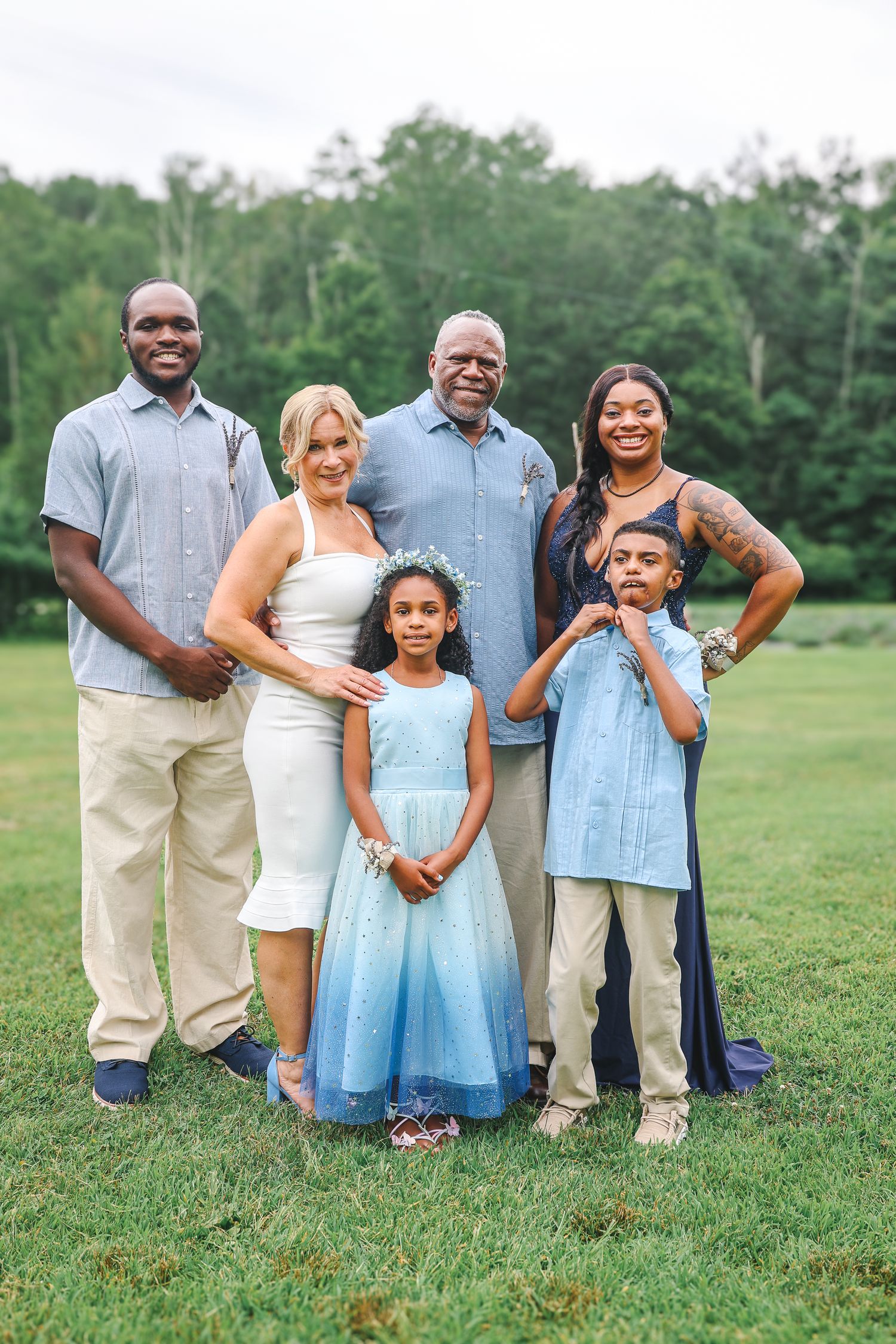 A family group poses together on green grass wearing coordinated blue and khaki outfits in a casual outdoor setting.
