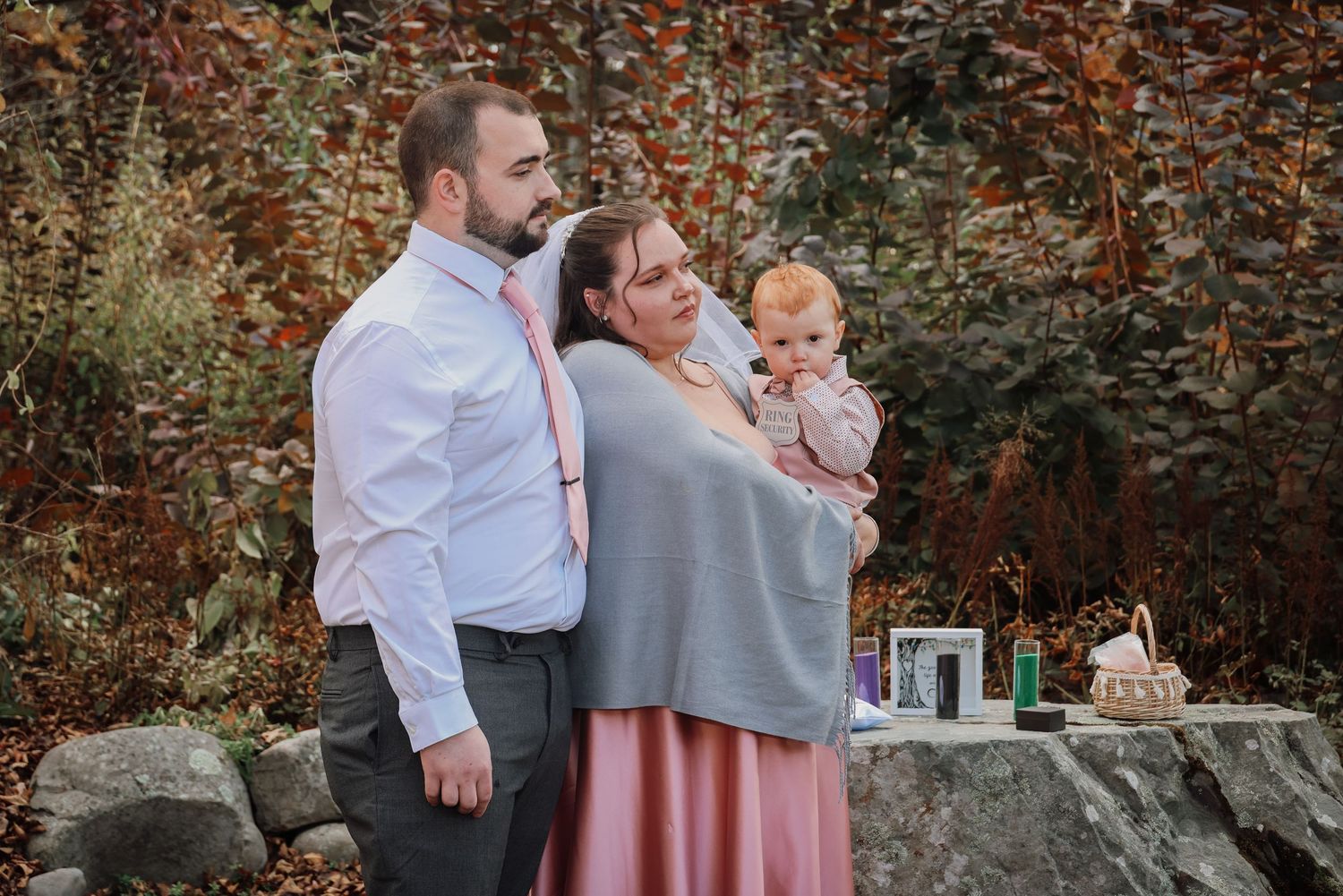A romantic couple shares a tender moment among autumn foliage and stone walls in an outdoor setting.