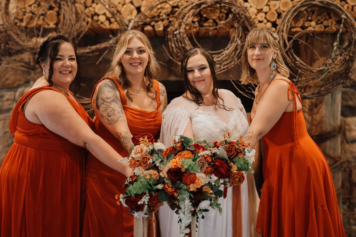 Wedding party in burnt orange bridesmaid dresses poses together holding floral bouquets in an outdoor setting.