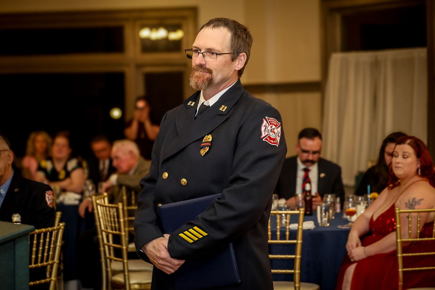 Firefighter in dress uniform holding a blue folder at a formal banquet ceremony event.