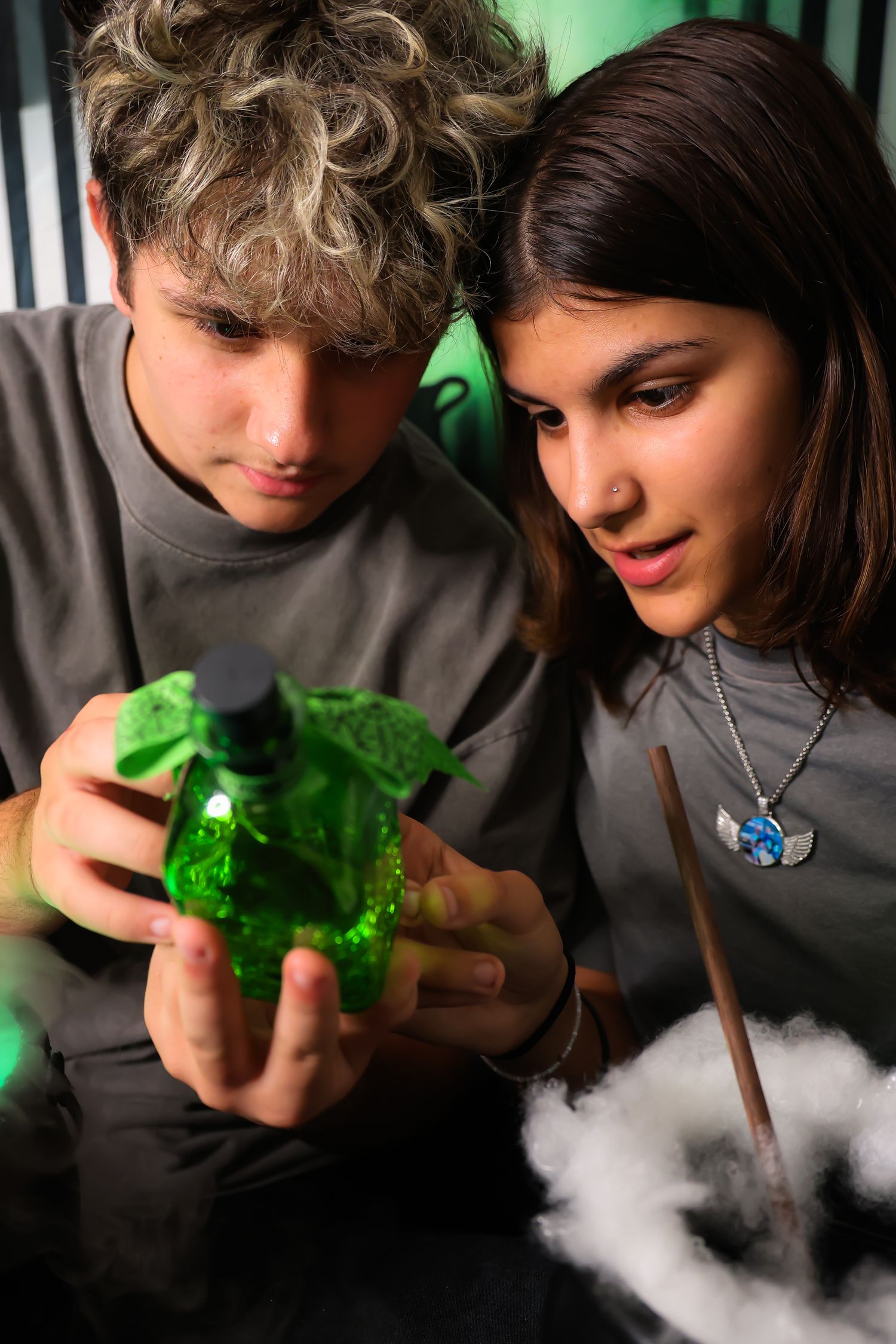 Two young people examining a green potion bottle with dry ice smoke effect at a Halloween party.