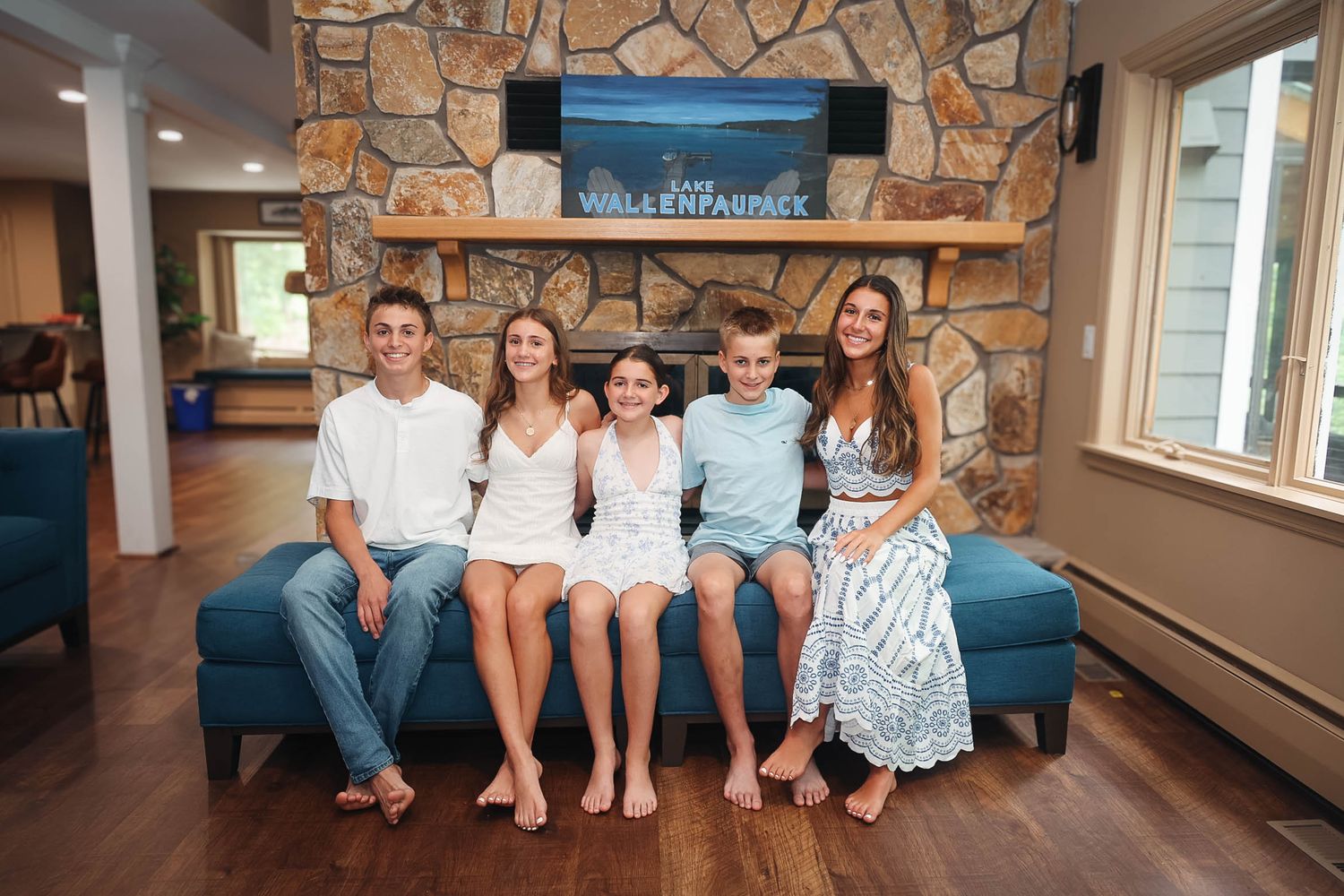 Five smiling family members sit together on a blue couch in front of a stone fireplace in a cozy living room.