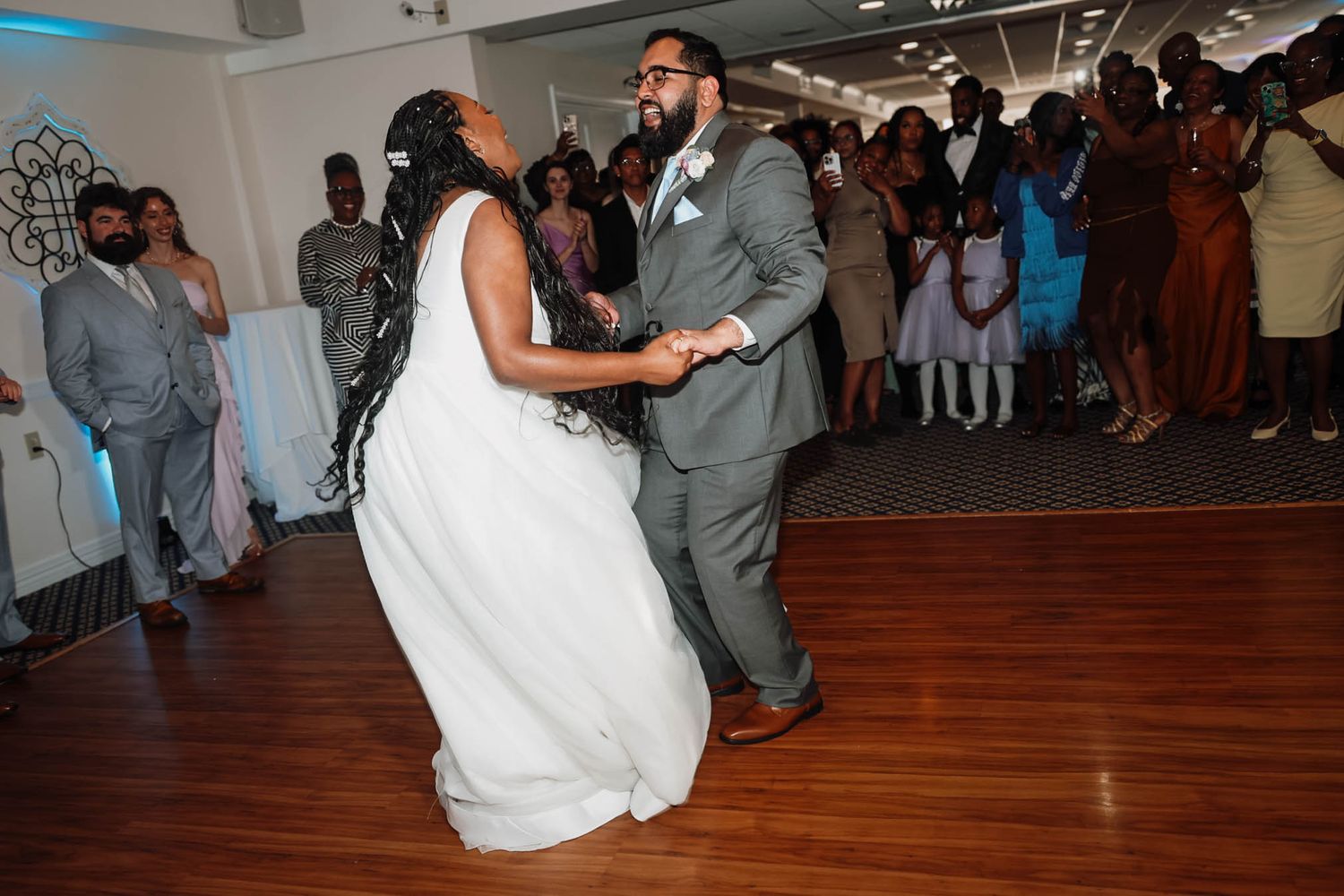 Bride and groom share their first dance at wedding reception, surrounded by guests in elegant venue.